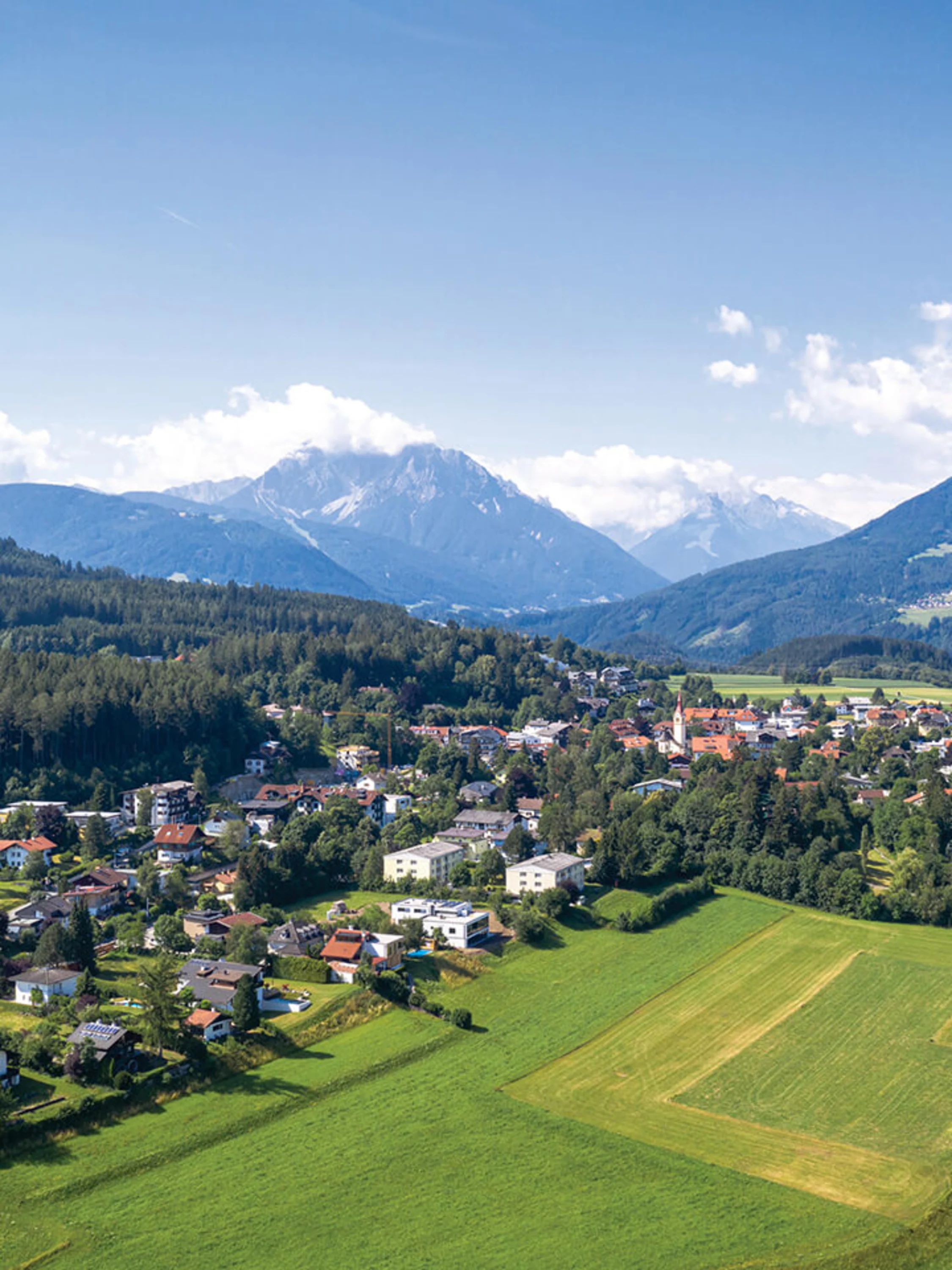 Foto: Ansicht Dorf Igls in Tirol mit grünen Feldern und Bergen im Hintergrund