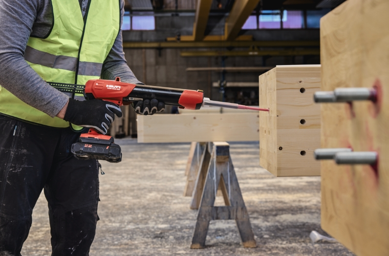 Ein Verarbeiter injiziert Klebstoff in vorbereitete Bohrlöcher eines Holzbauteils und bereitet damit die Montage eingeklebter Gewindestangen im Ingenieurholzbau vor.
