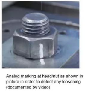 Close-up of a bolted steel connection with a white paint mark spanning the nut and steel plate. The alignment mark provides a visual indication of any loosening by showing movement between the nut and the base material.