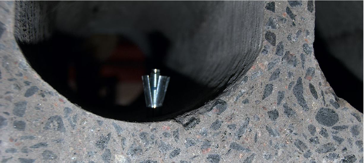 Närbild av ett håldäcksbjälklag i betong med synlig hålkanal och en metallisk infästning monterad i betongen. Bilden illustrerar infästningsplacering och betongtjocklek i håldäck.
