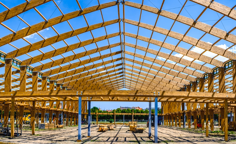Großes Holztragwerk im Bauzustand mit weitgespannter Dachkonstruktion, regelmäßigen Stützenreihen und sichtbar verbauten Holzträgern einer Ingenieurholzbaukonstruktion.
