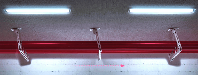 Chemin de câbles rouge Hilti fixé au plafond béton par des supports métalliques ancrés, avec éclairage intégré