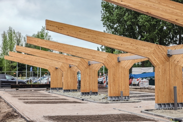 Holzkonstruktion im Bau mit Brettschichtholzrahmen und geneigten Trägern auf Betonfundamenten in einem Außenbereich.