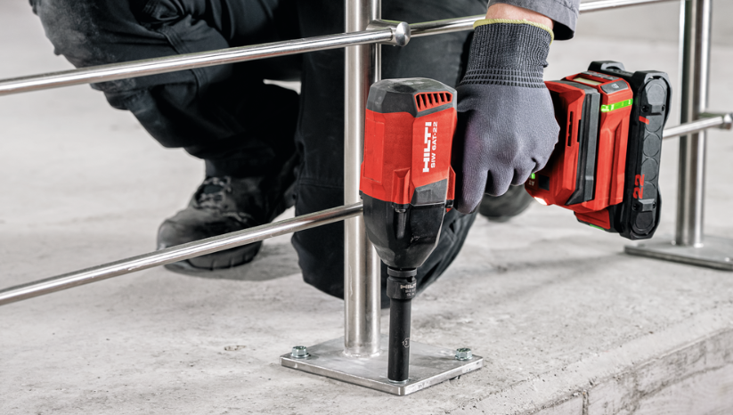 Person använder en batteridriven Hilti mutterdragare för att dra åt en förankringsbult i fotplattan på ett räcke av rostfritt stål som är monterat i ett betonggolv.