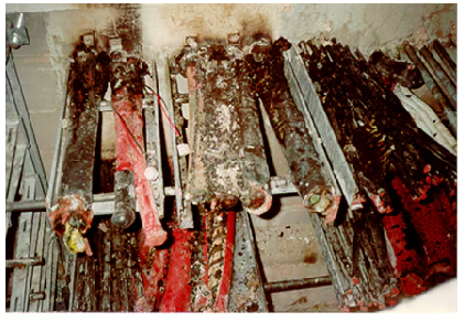 Post fire test setup with cable trays densely packed with cables and numerous red wires draped and tangled across a metal frame, illustrating a complex cable installation scenario. Showing the damage after the fire.