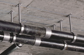 Parallelle leidingen bevestigd aan een betonnen plafond met metalen buisklemmen en draadeinden als niet-dragende installatieconstructie.