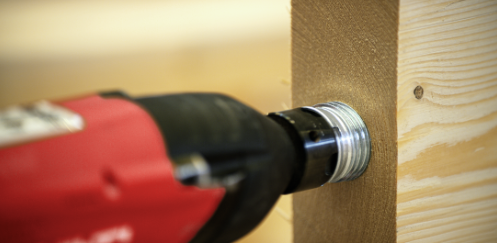 Close-up of a power tool installing a threaded metal connector into a timber beam, highlighting a timber-to-steel connection detail used in timber construction.