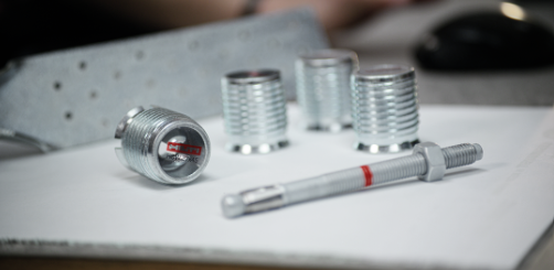 Close-up of threaded metal connectors and an installation rod arranged on a work surface, highlighting connection components used in structural timber construction.