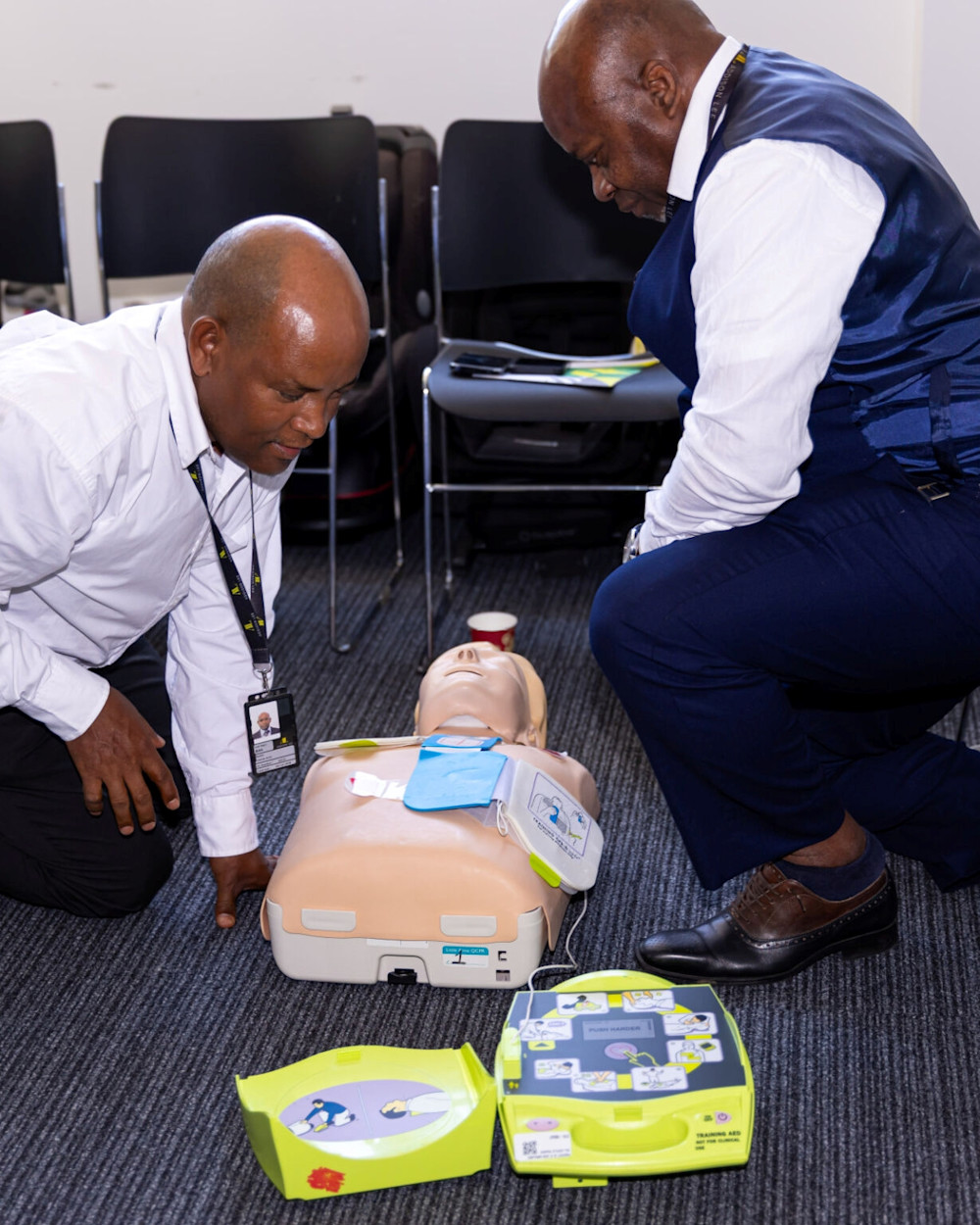 Two Addison Lee drivers leaning over a manikin while taking part in CPR and defibrillator training sessions.