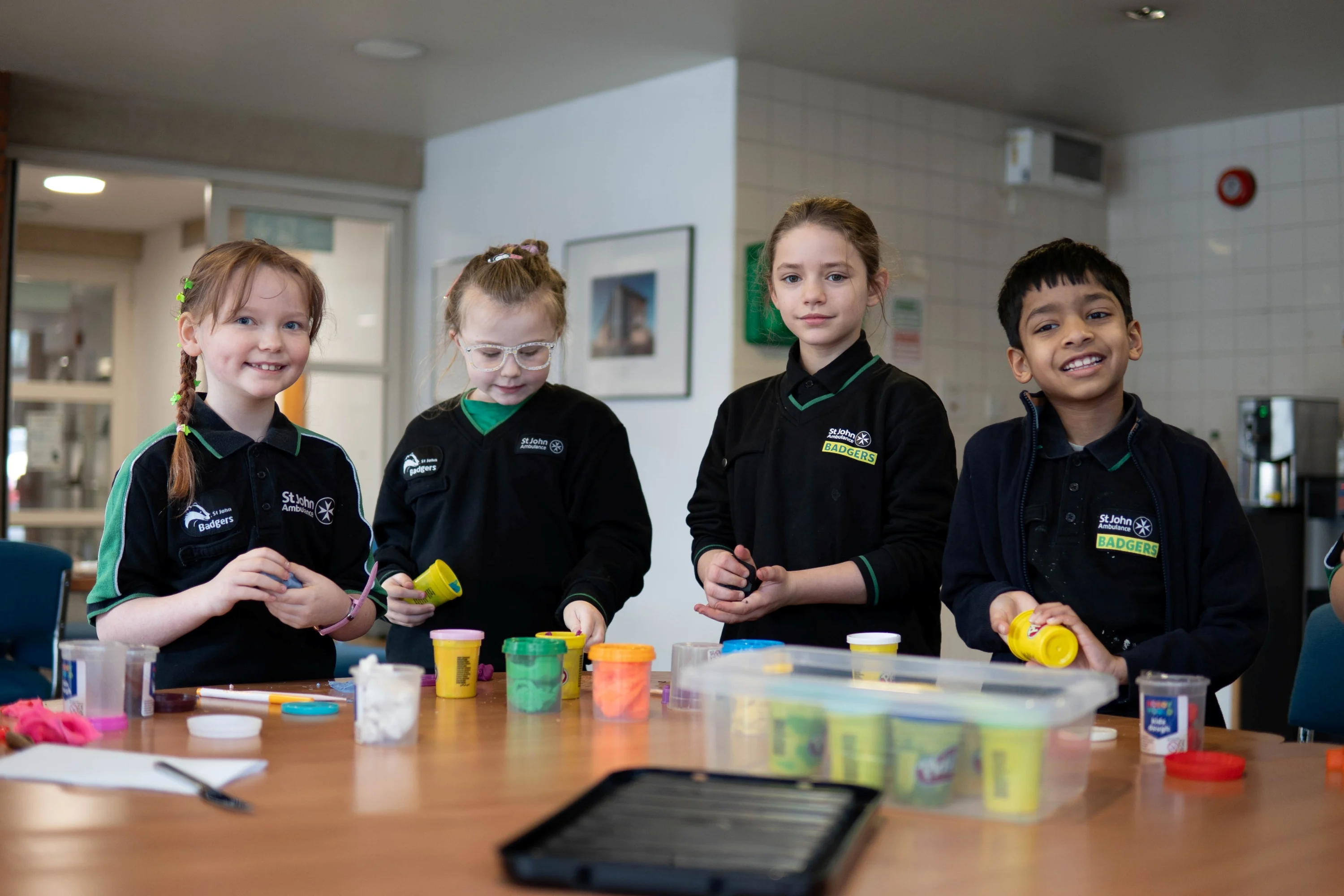 Four Badgers standing at a table with lots of playdough pots on it.