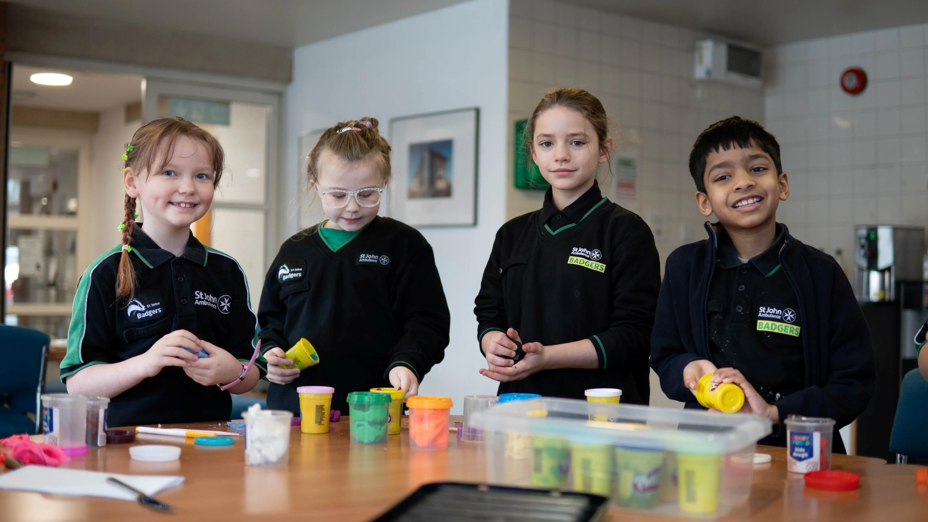 Four Badgers standing at a table with lots of playdough pots on it.