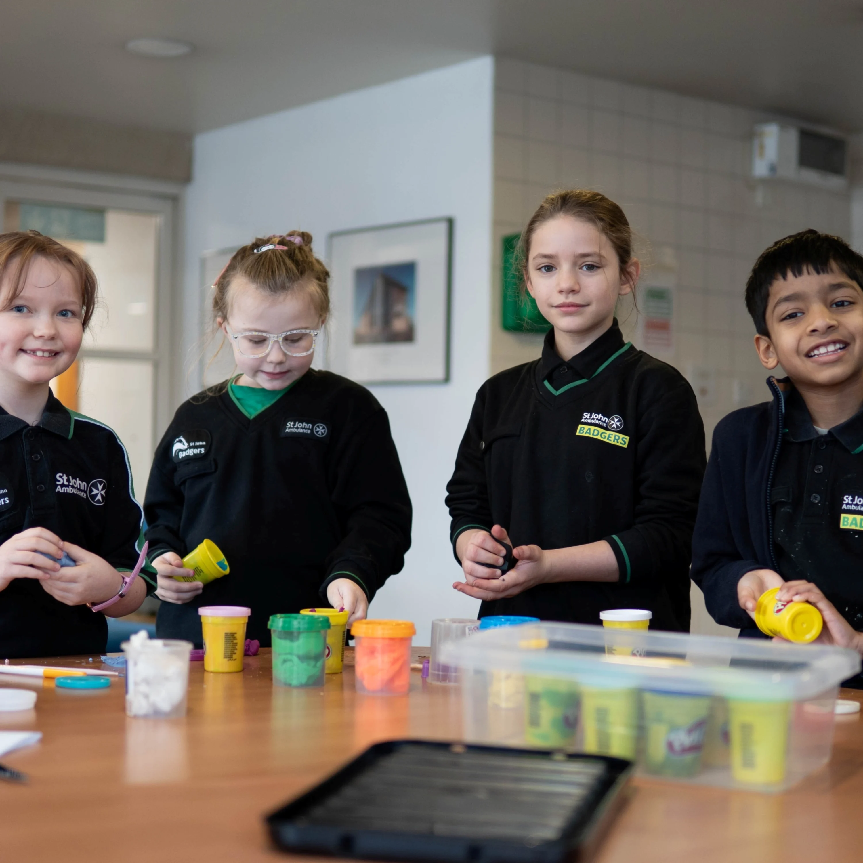 Four Badgers standing at a table with lots of playdough pots on it.