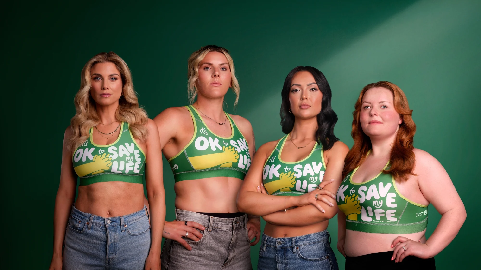 A photograph of Ashley James, Millie Bright, Sharon Gafka and Lucy Edwards (from left to right), wearing St John Ambulance's CPR Bras, standing in front of a dark green backdrop.