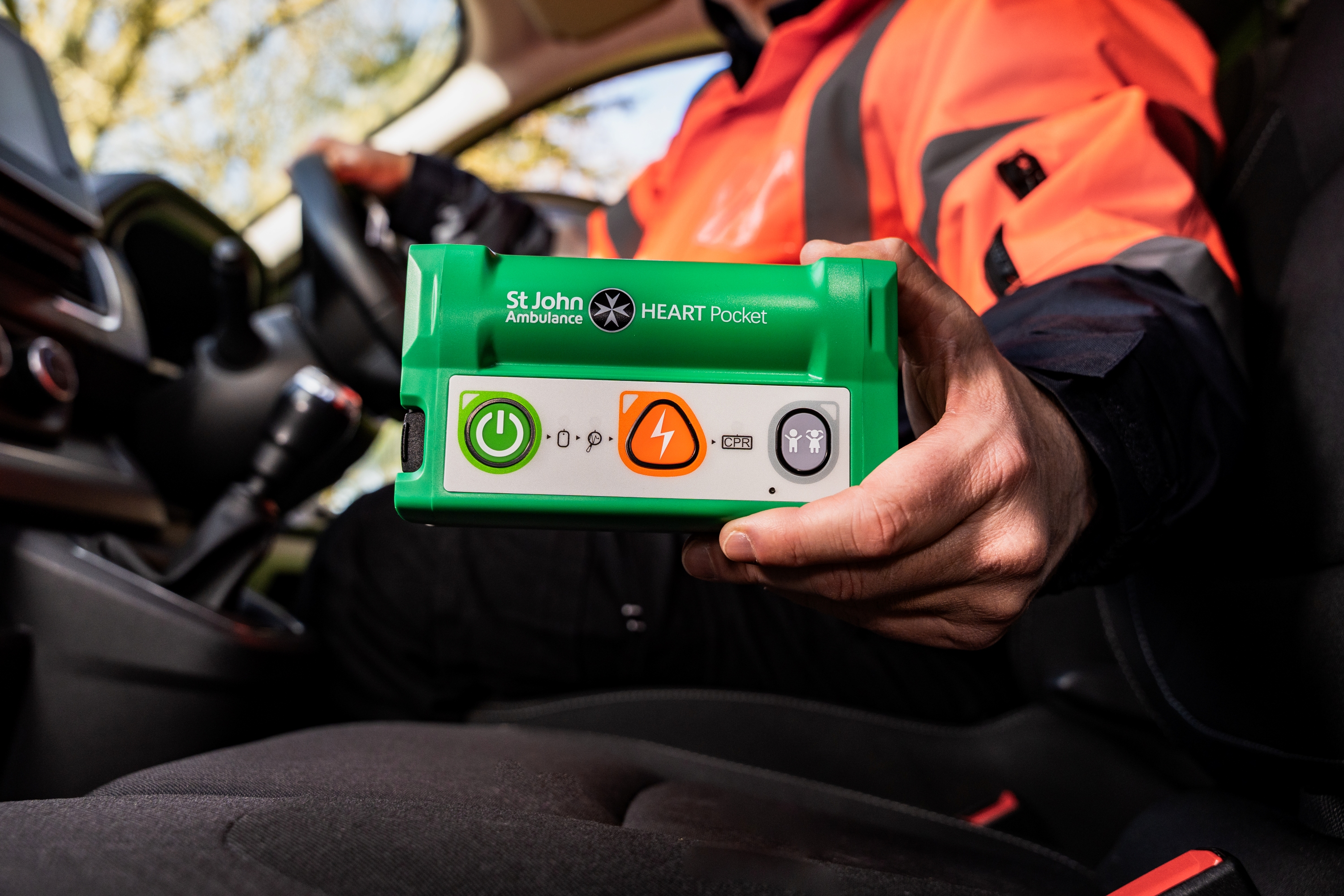 A remote working in a van, holding the HEART Pocket defibrillator in one hand, demonstrating the portability.