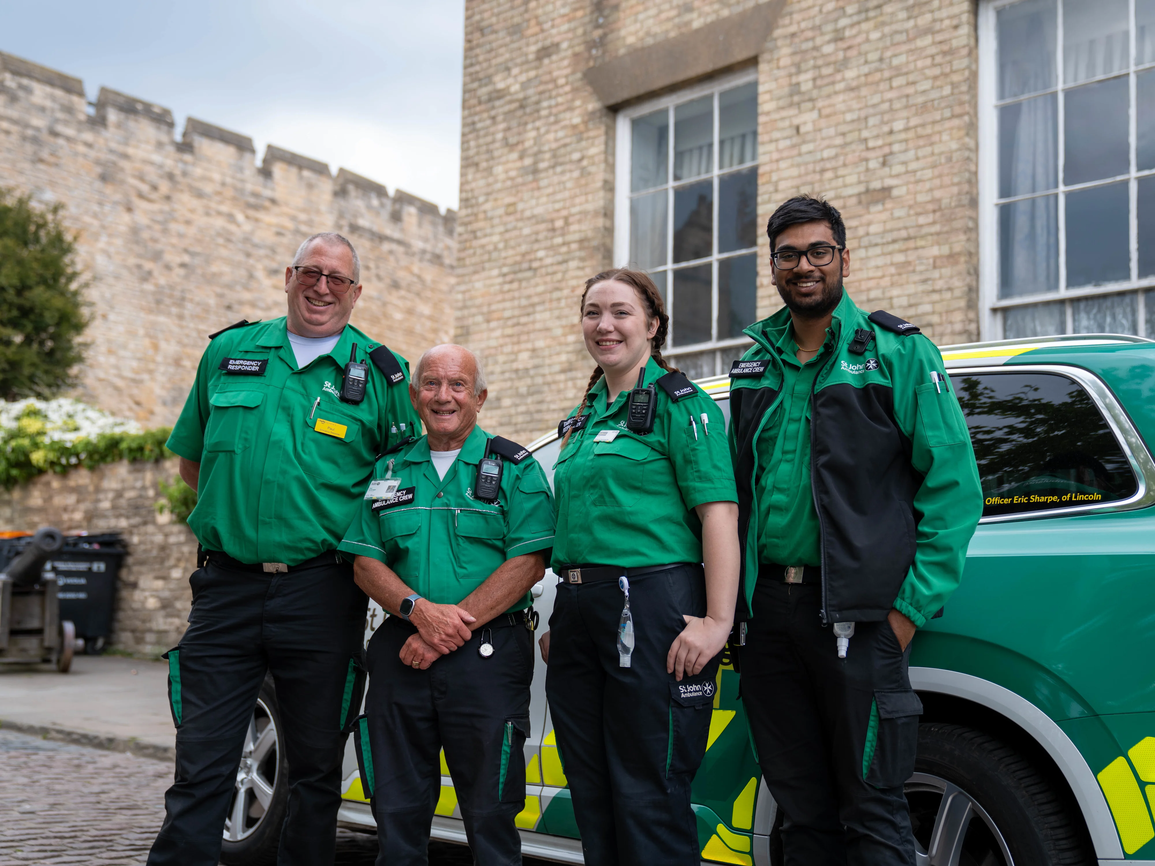 Four St John Ambulance volunteers stood smiling in front of an emergency responder vehicle.