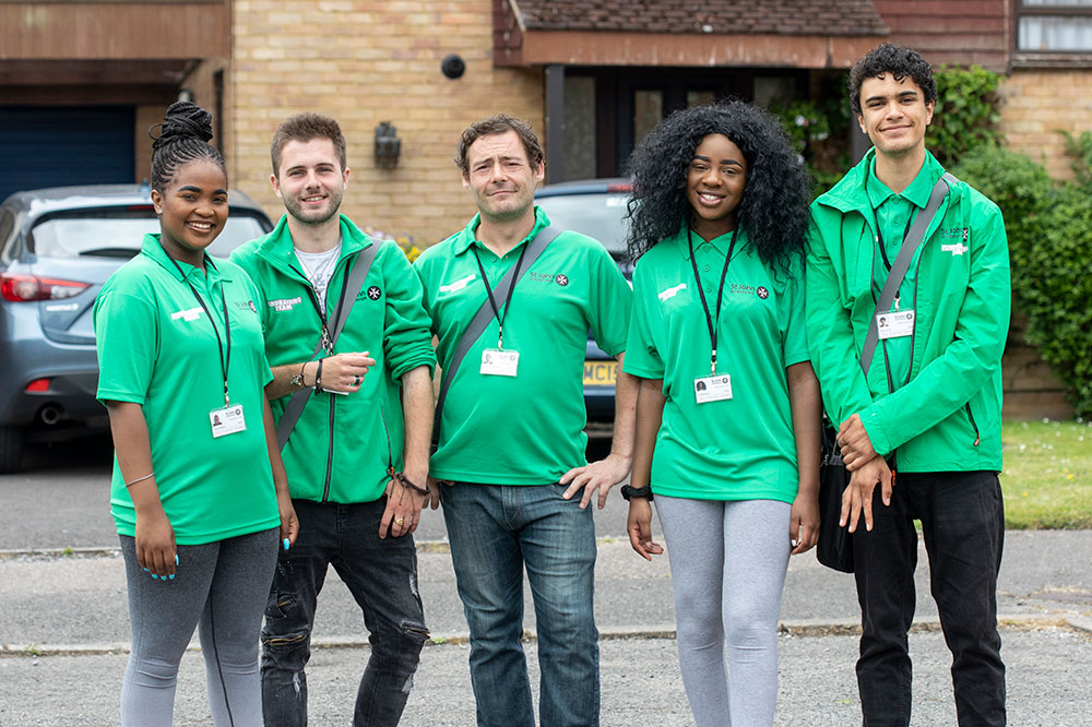 Five people wearing St John Ambulance face-to-face fundraising uniform stood on a road. Behind them are houses and parked cars. 