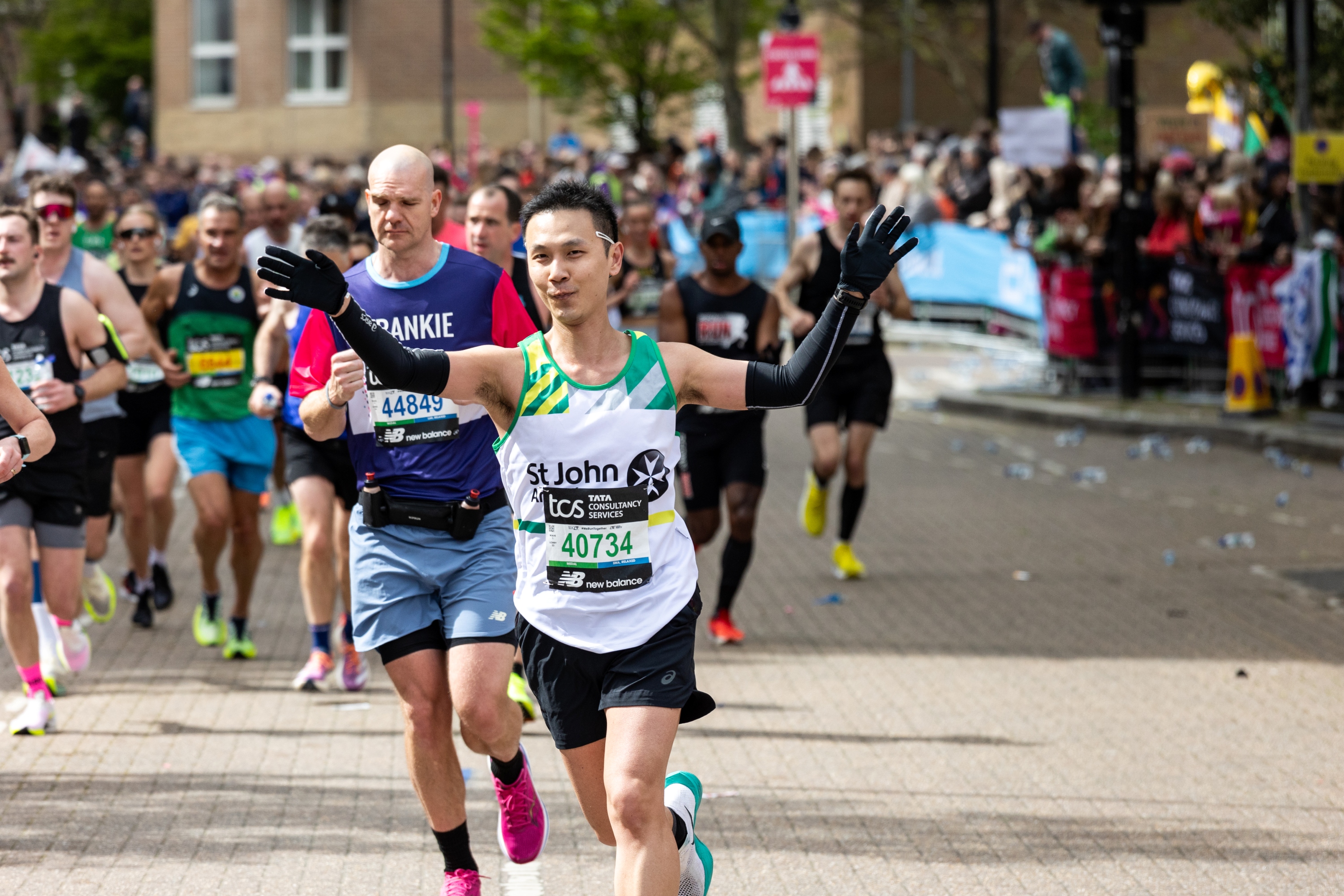 Marathon runners, with one taking part for St John Ambulance, holding both arms in the air.