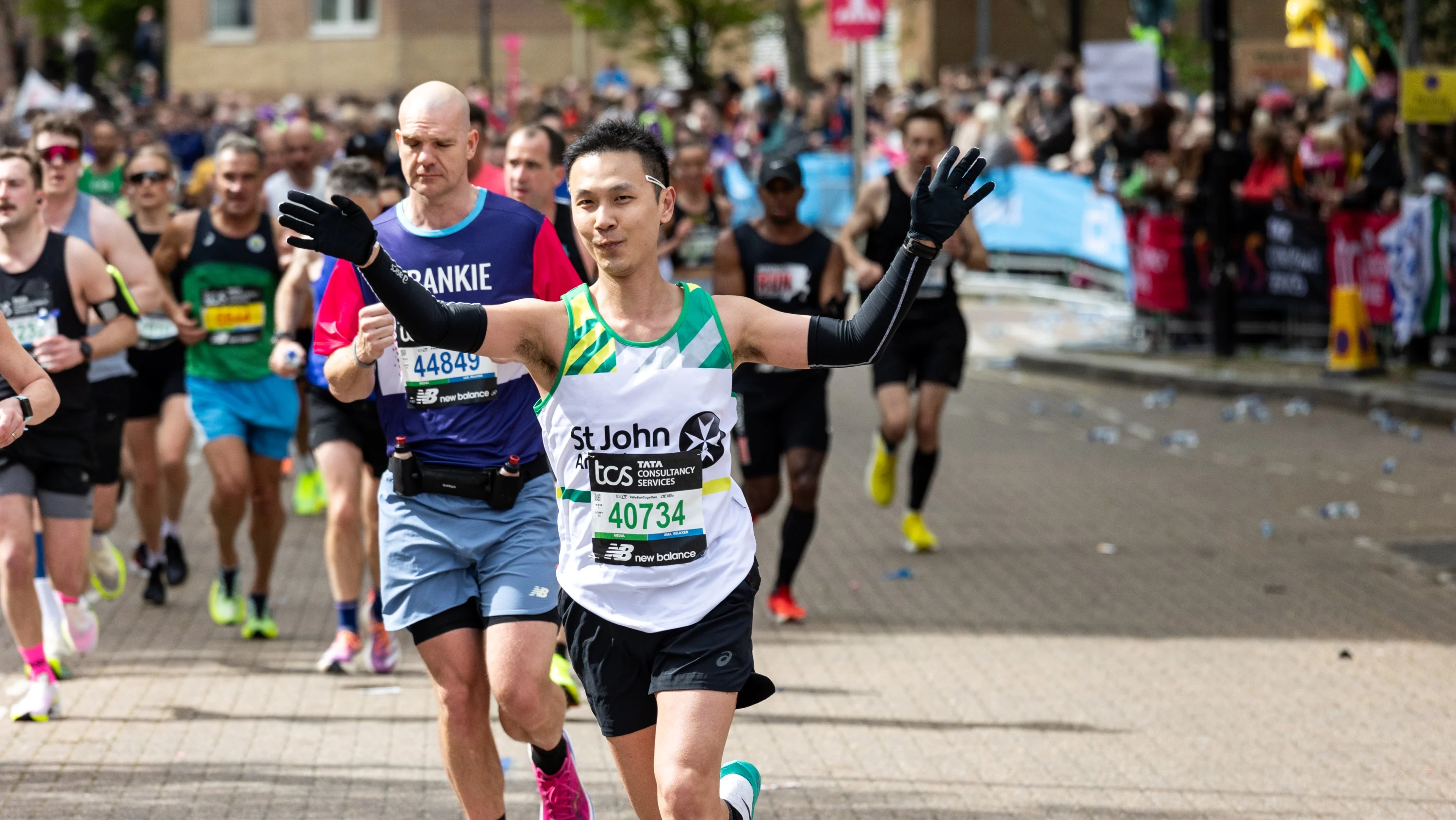 Marathon runners, with one taking part for St John Ambulance, holding both arms in the air.