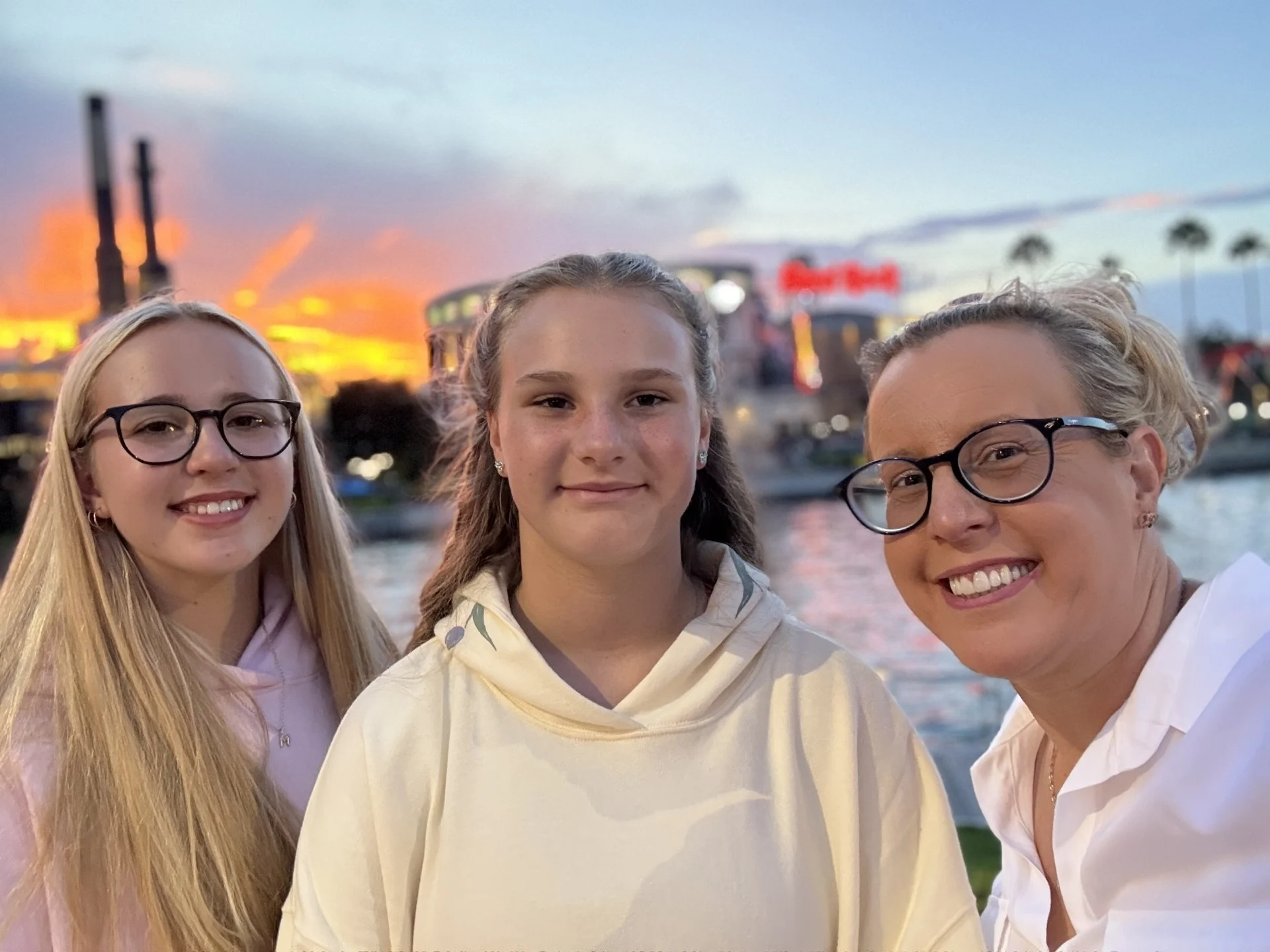 Laura, Hollie, and Maisie in a photograph together, smiling with a sunset in the background.