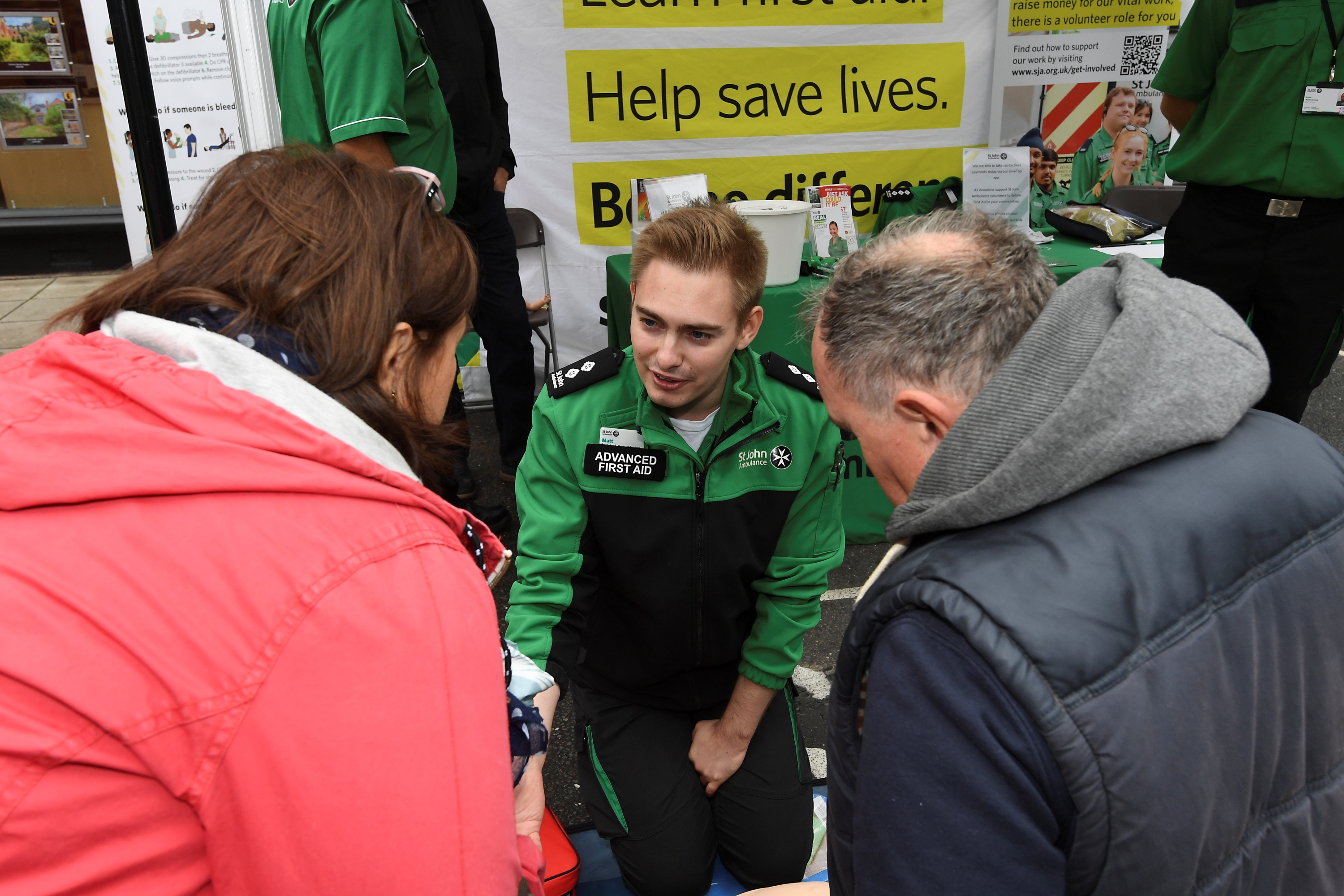 A first aider kneeling down, giving two people some first aid training and advice.