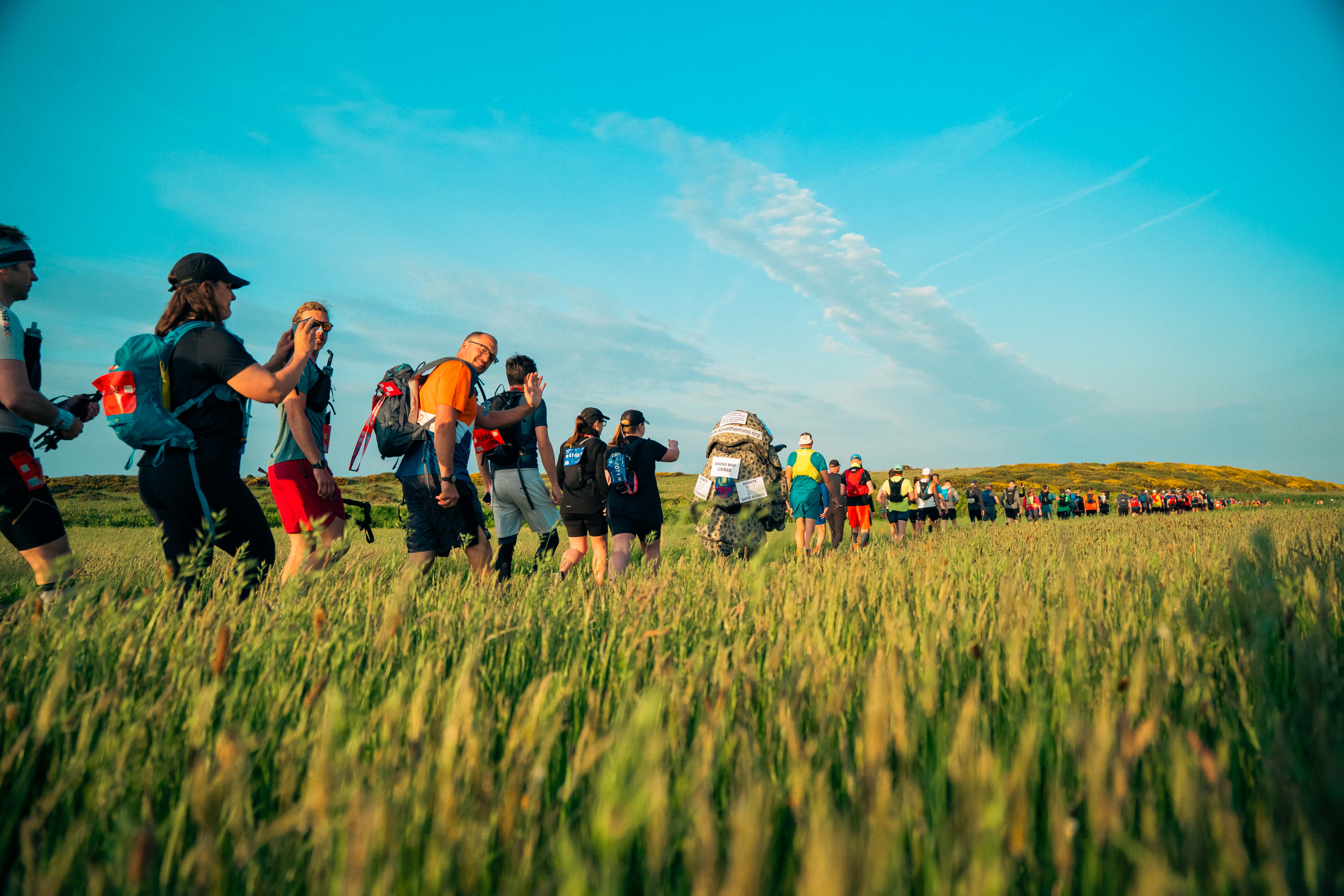 Group of people in active wear and backpacks walking across a field in a single line.