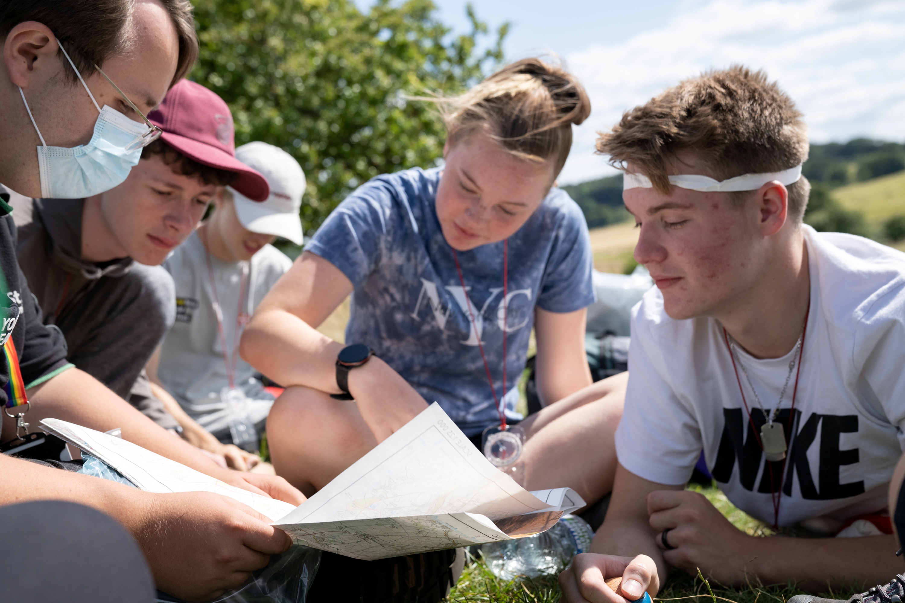 Five people outside sat down in a field looking at a map.