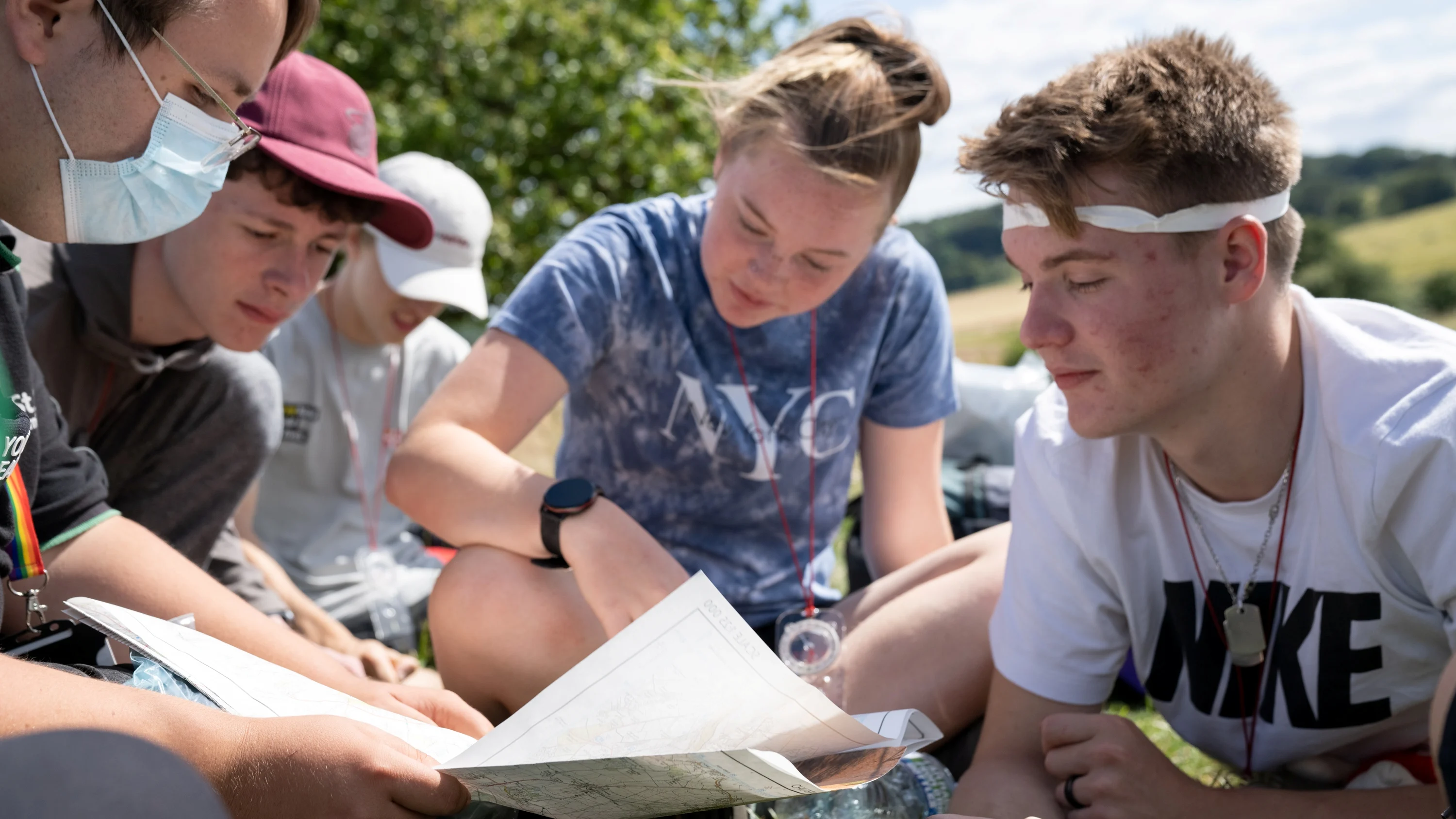Five people outside sat down in a field looking at a map.