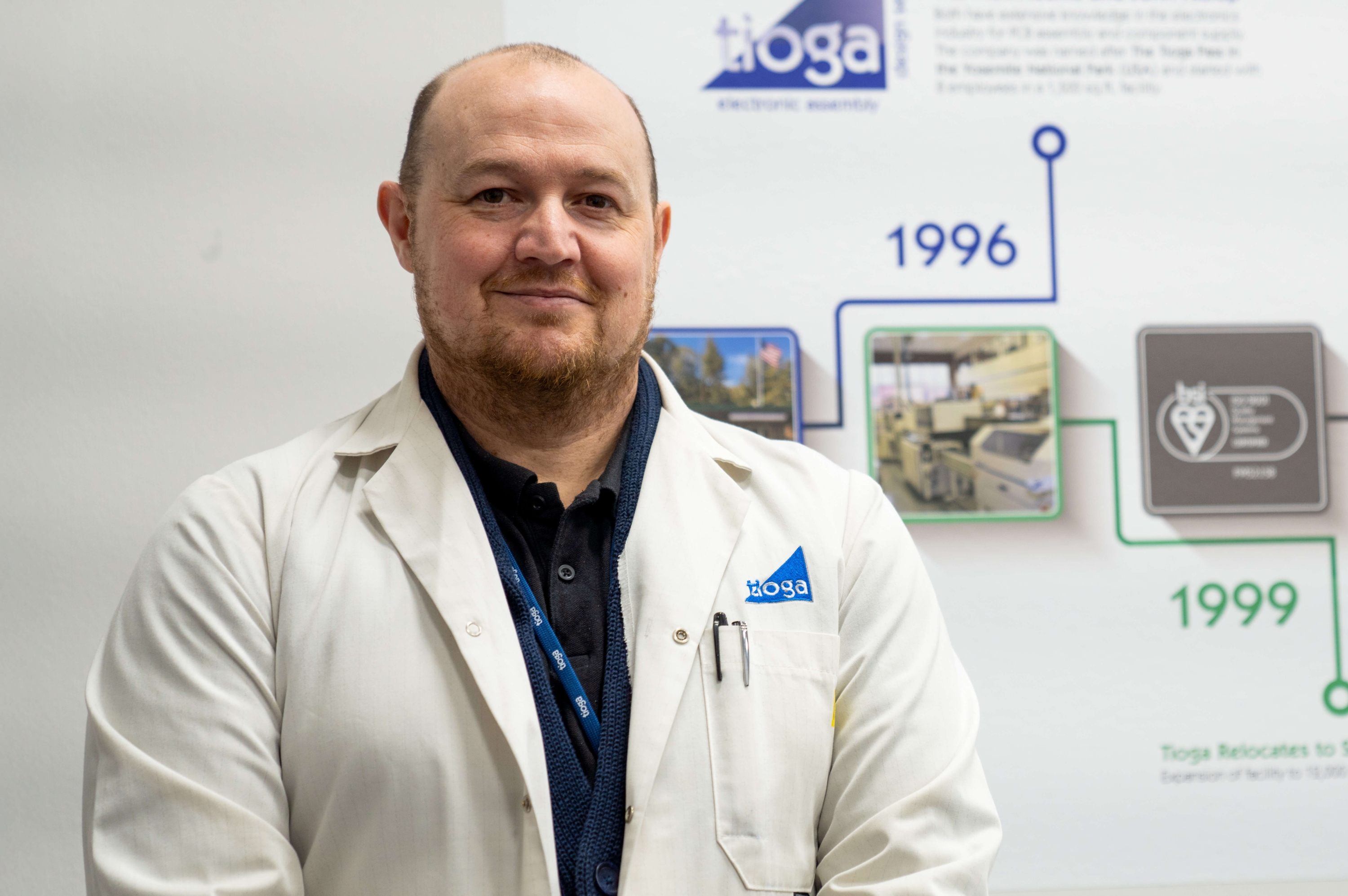 A photograph of Shaun Cardwell wearing a lab coat and smiling at the camera.