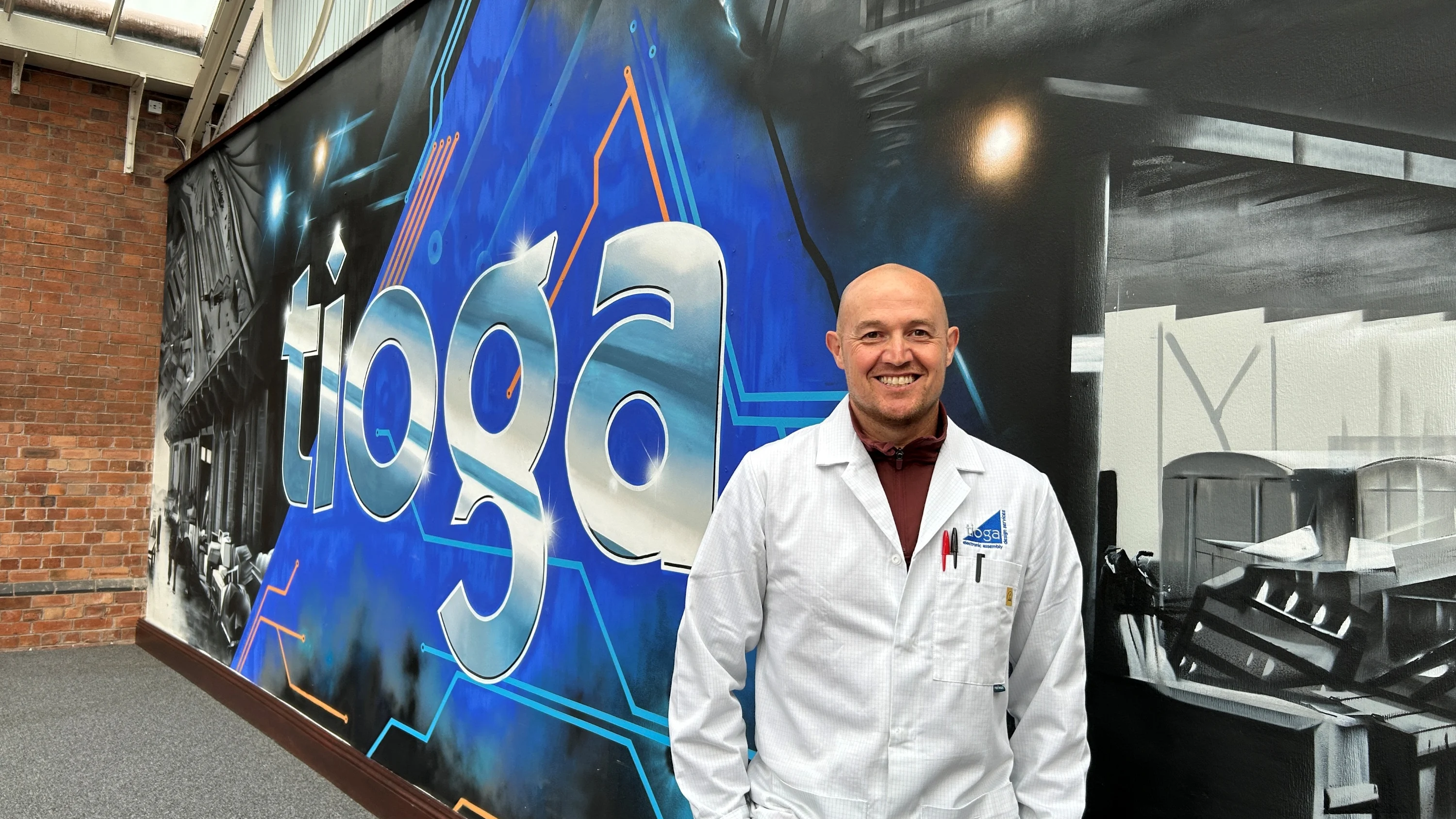 A photograph of Shaun Cardwell wearing a lab coat and smiling at the camera.