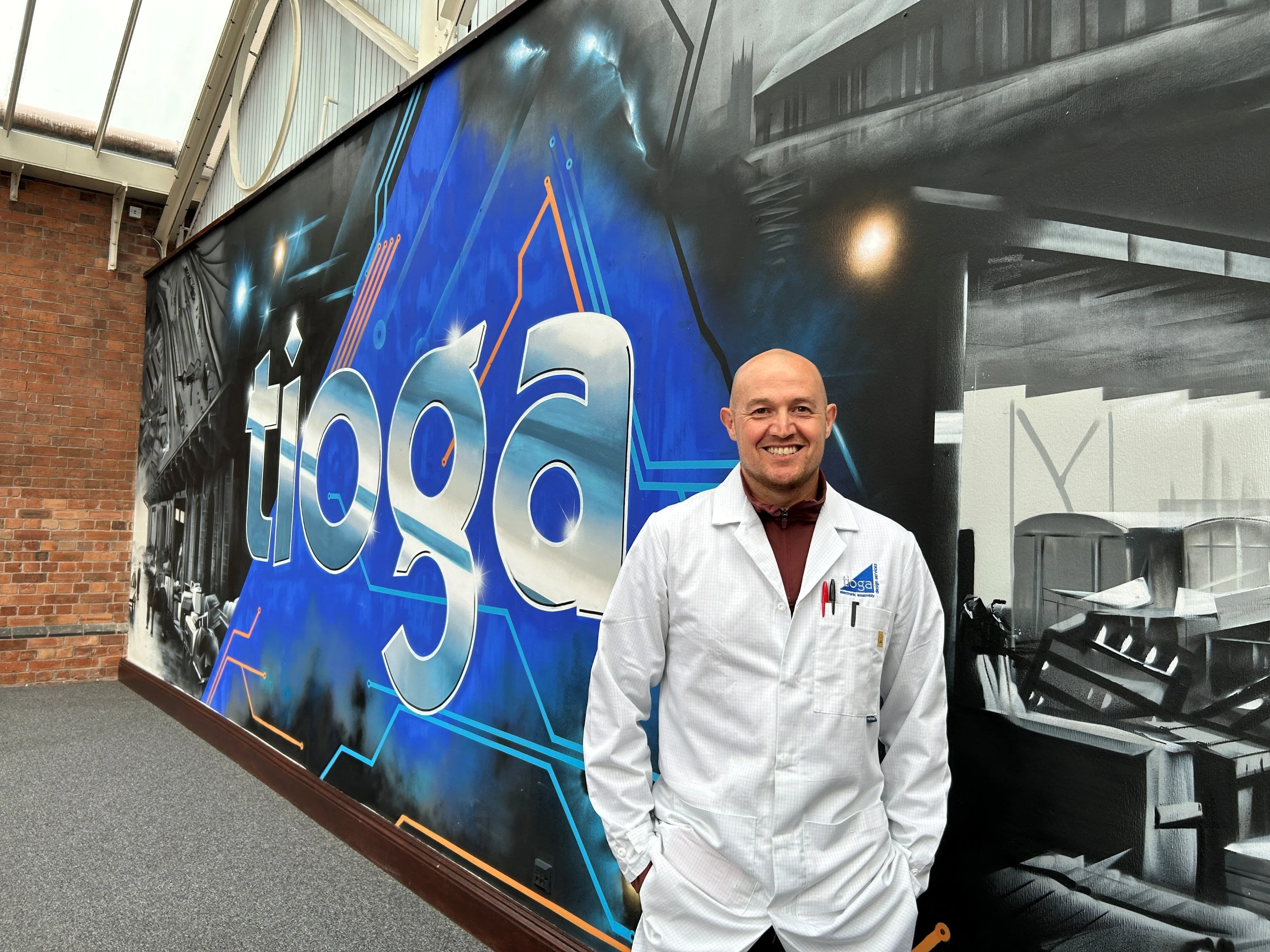 A photograph of Shaun Cardwell wearing a lab coat and smiling at the camera.