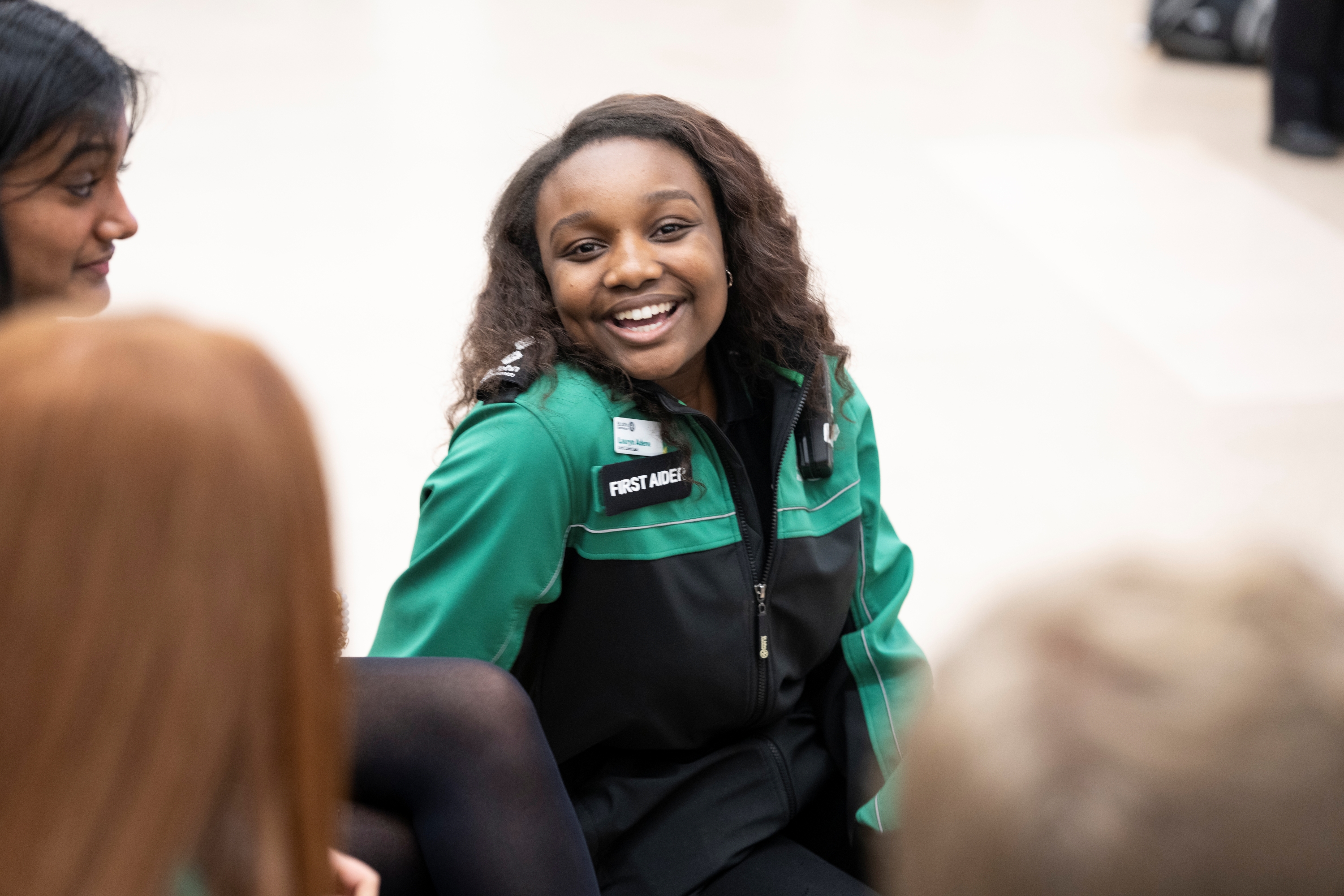 A First Aid volunteer with a big smile sat on the floor in front of three other people. 