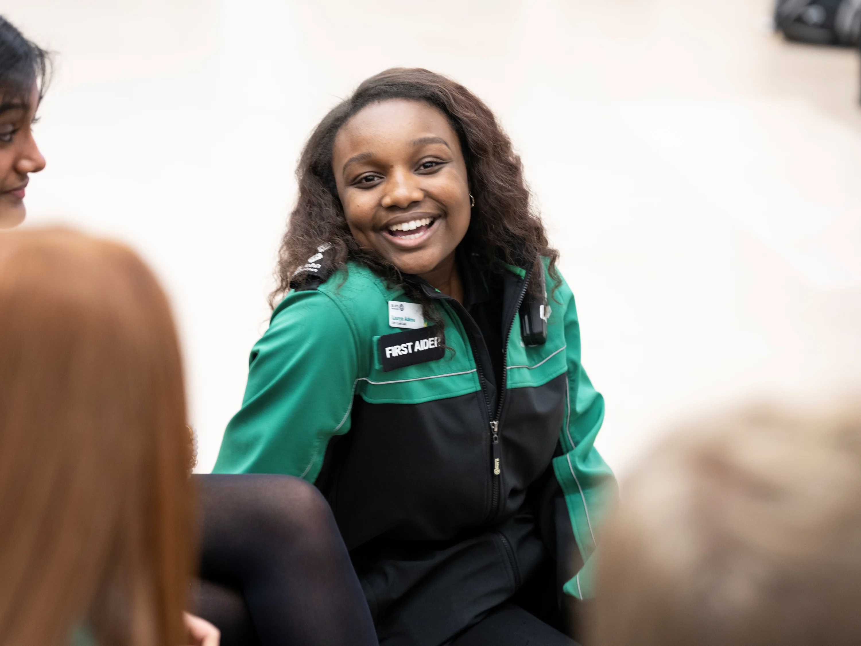 A First Aid volunteer with a big smile sat on the floor in front of three other people.
