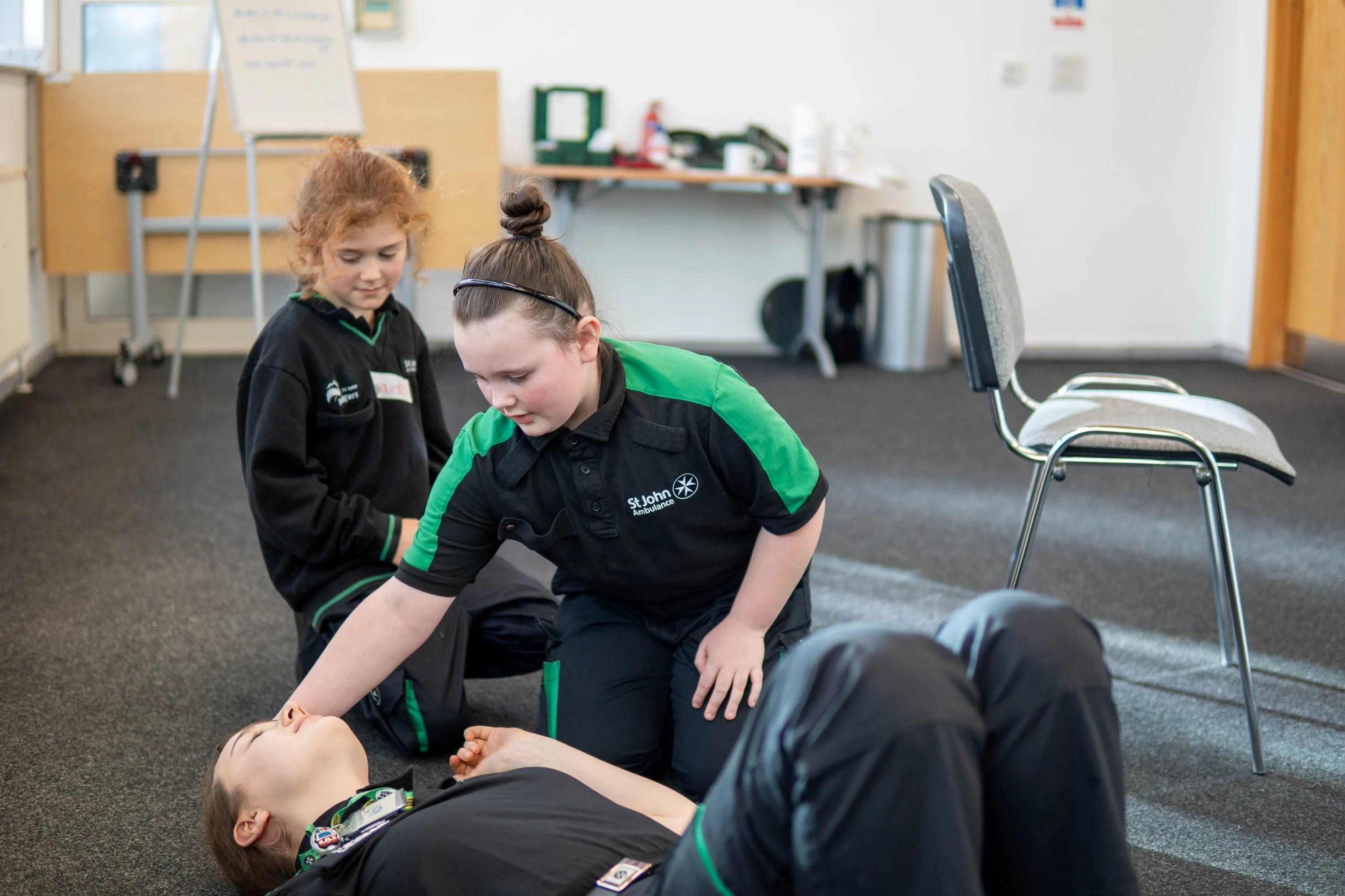 Two Badgers kneeling on the floor. One is leaning over an adult lying on the floor with their hand on the top of their head.