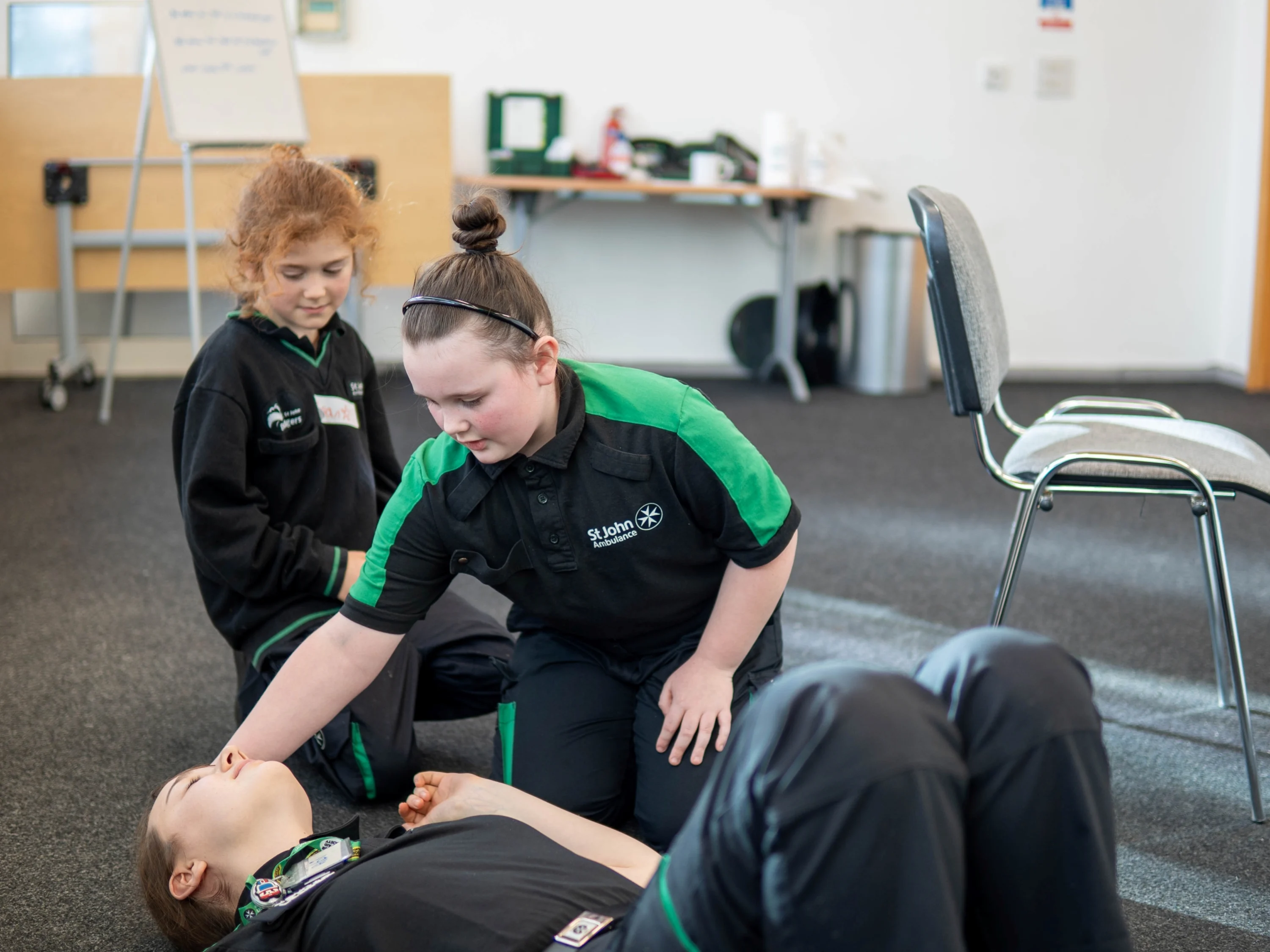 Two Badgers kneeling on the floor. One is leaning over an adult lying on the floor with their hand on the top of their head.