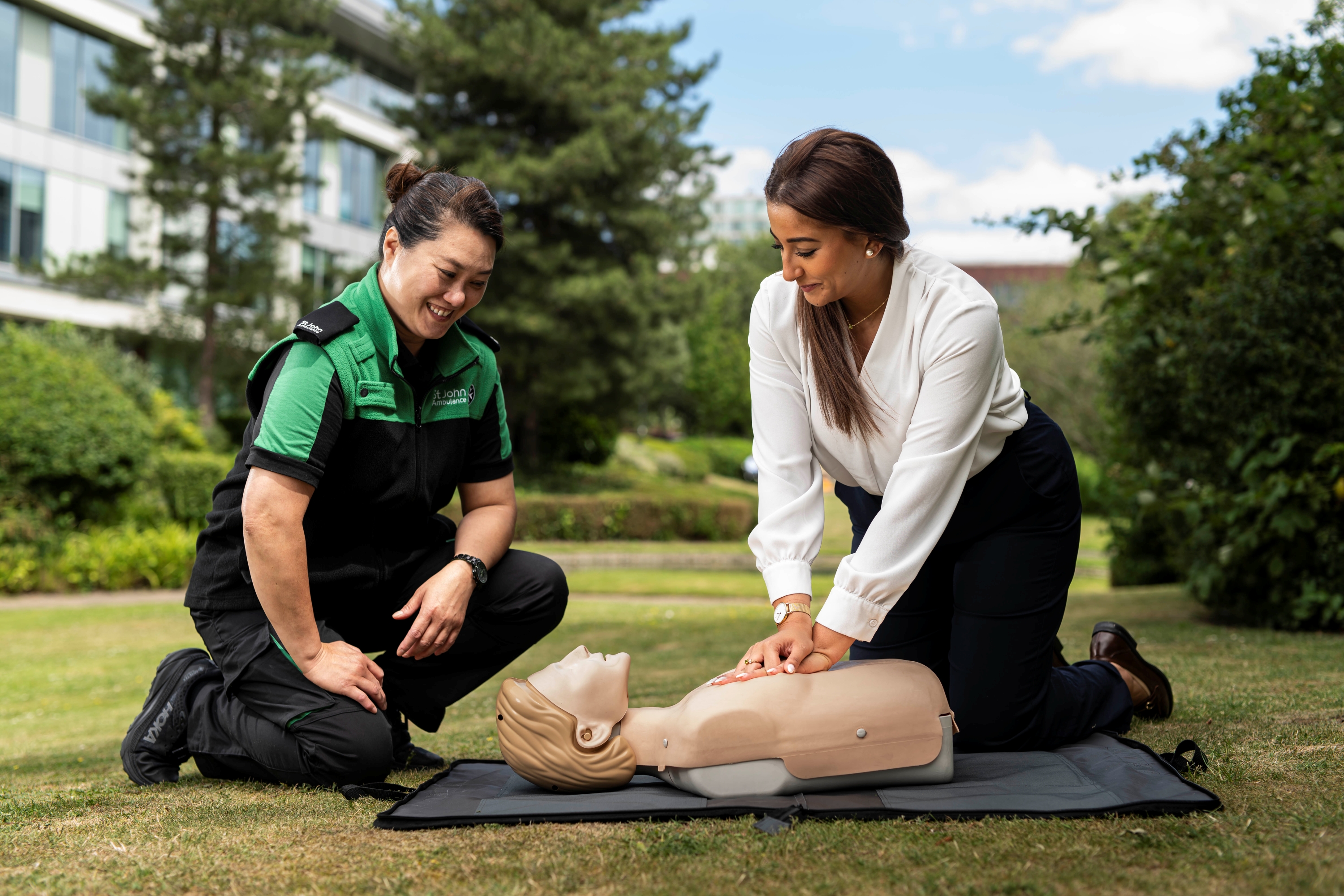 A St John Ambulance trainer with someone learning first aid, practicing chest compressions on a manikin.