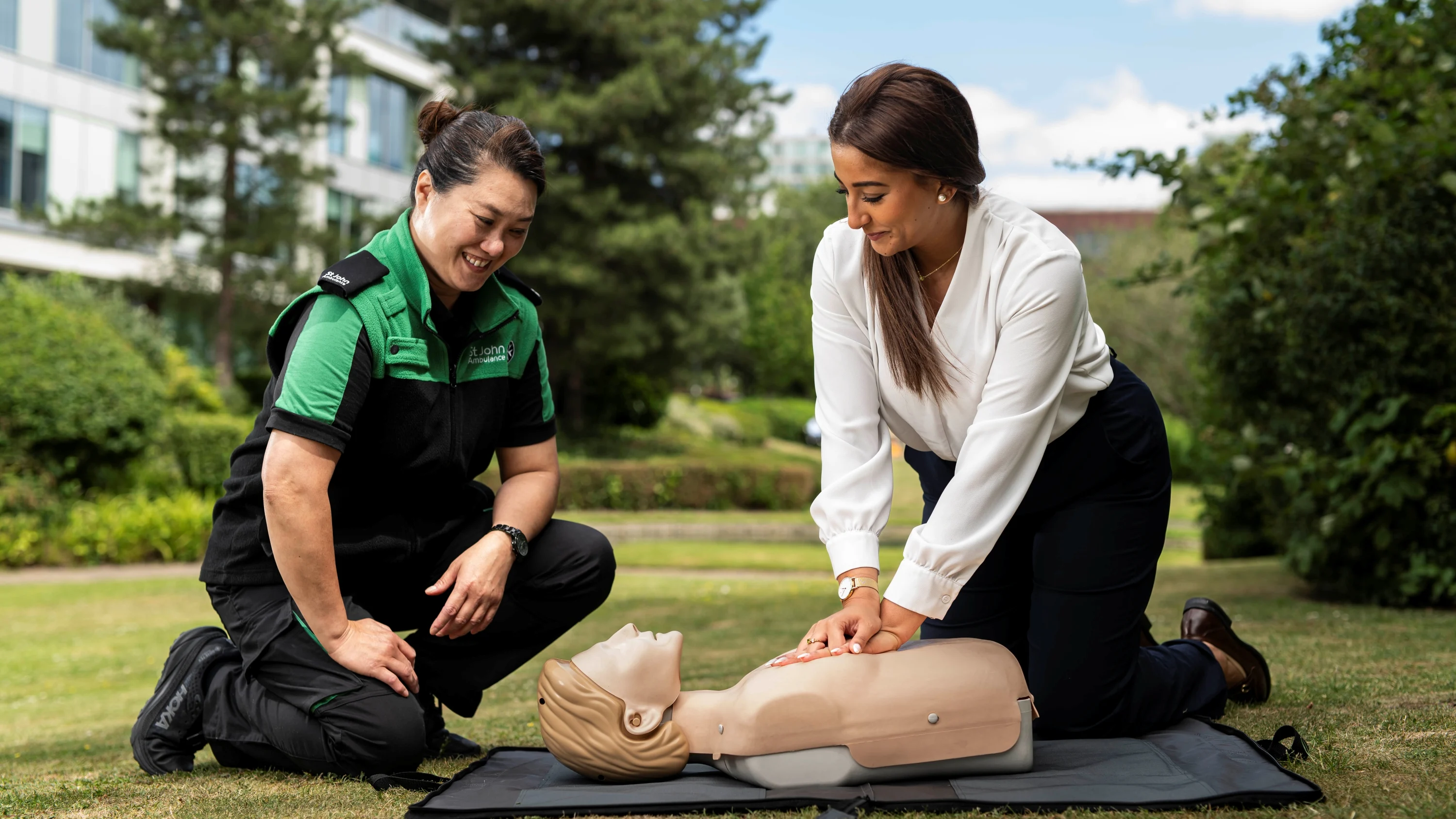 A St John Ambulance trainer with someone learning first aid, practicing chest compressions on a manikin.