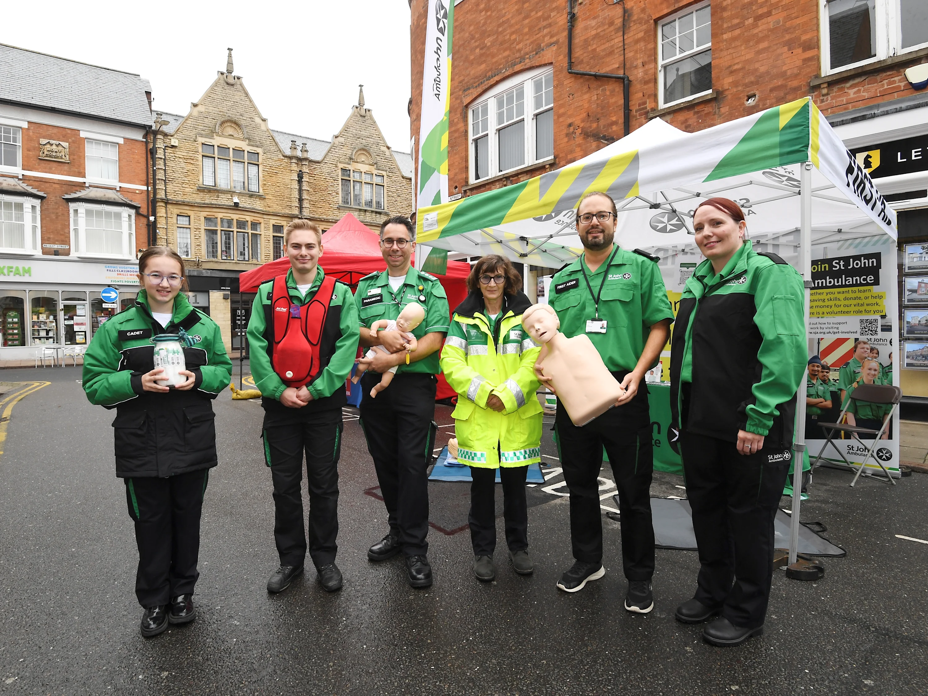 A group of six St john Ambulance first aid trainers in uniform, holding training equipment.