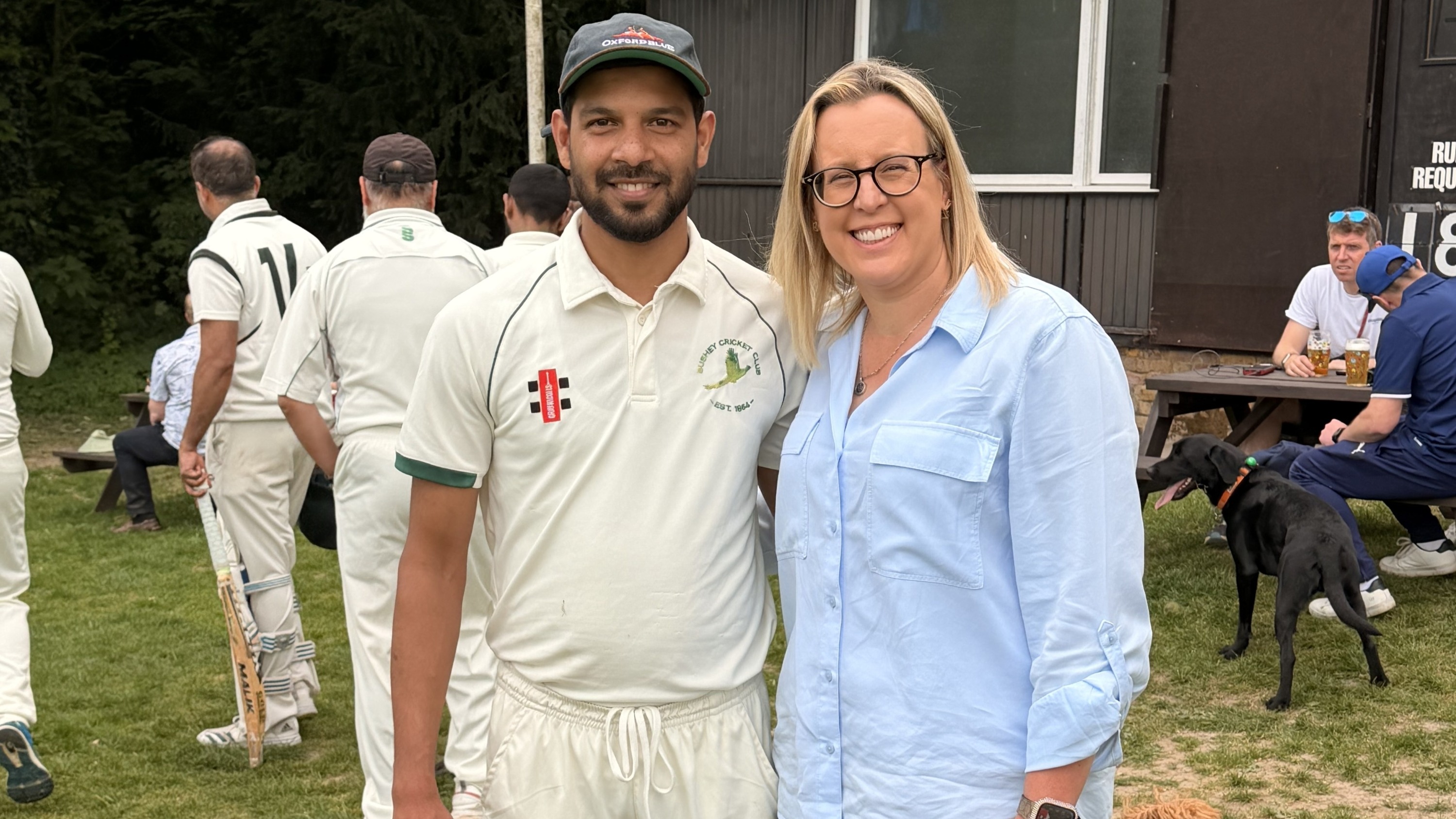 Laura and Hussain posing together at a cricket club and smiling for the camera.