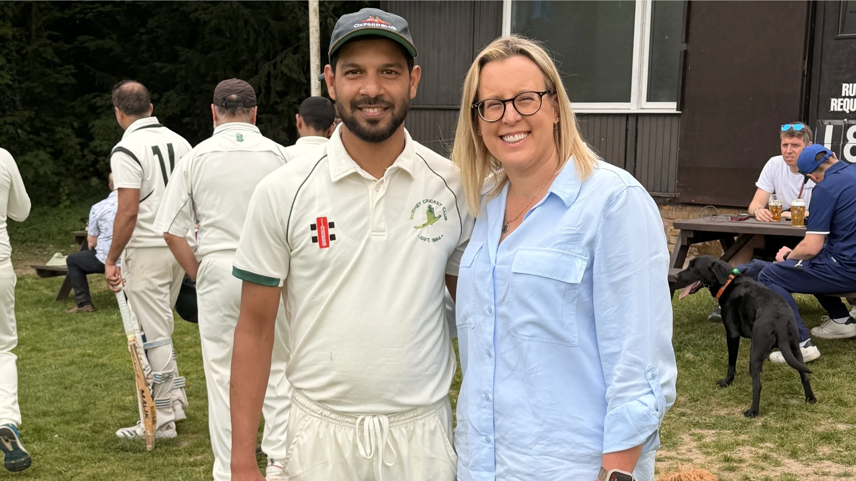 Laura and Hussain posing together at a cricket club and smiling for the camera.