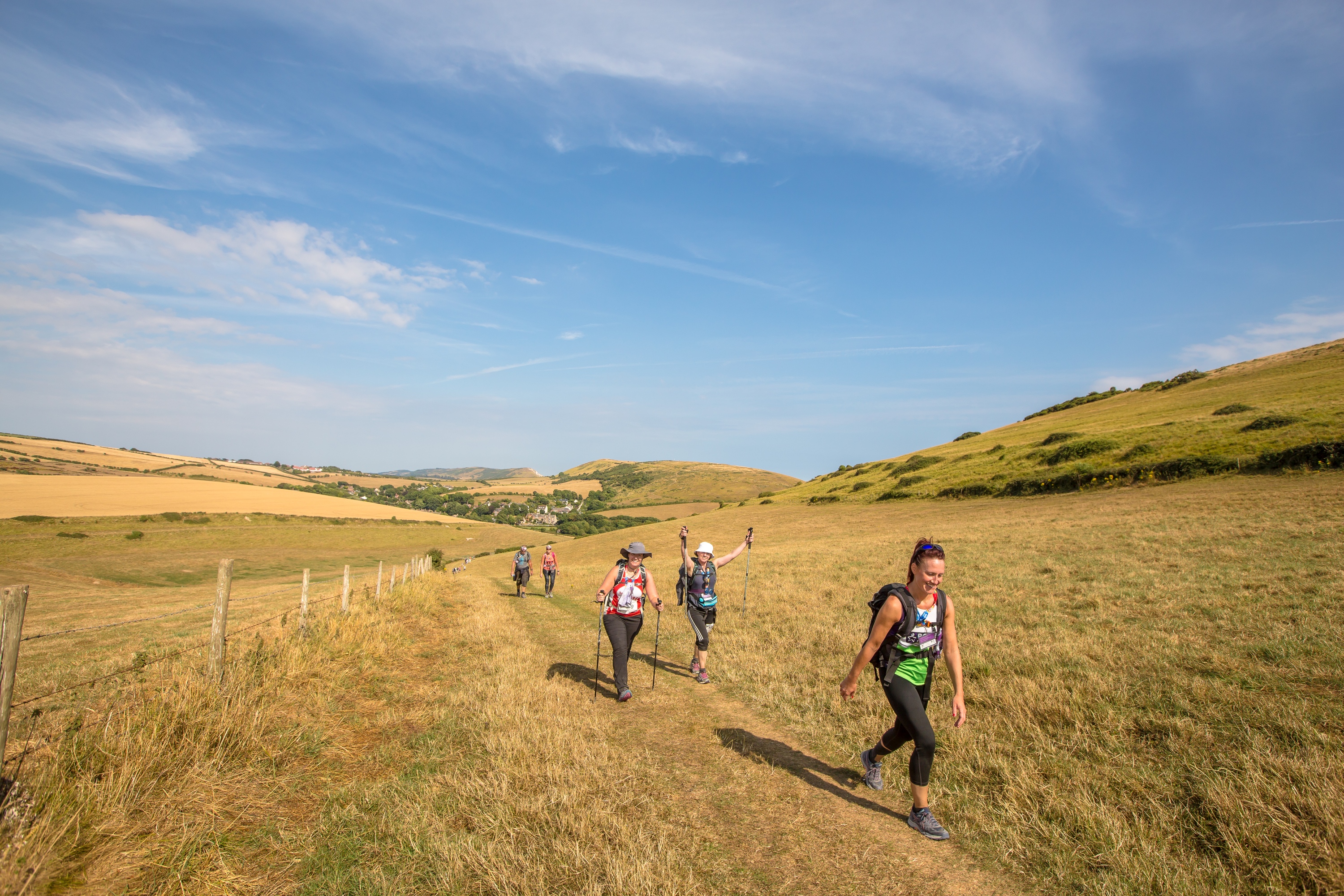 Five people walking across an open field with buildings and hills in the background.
