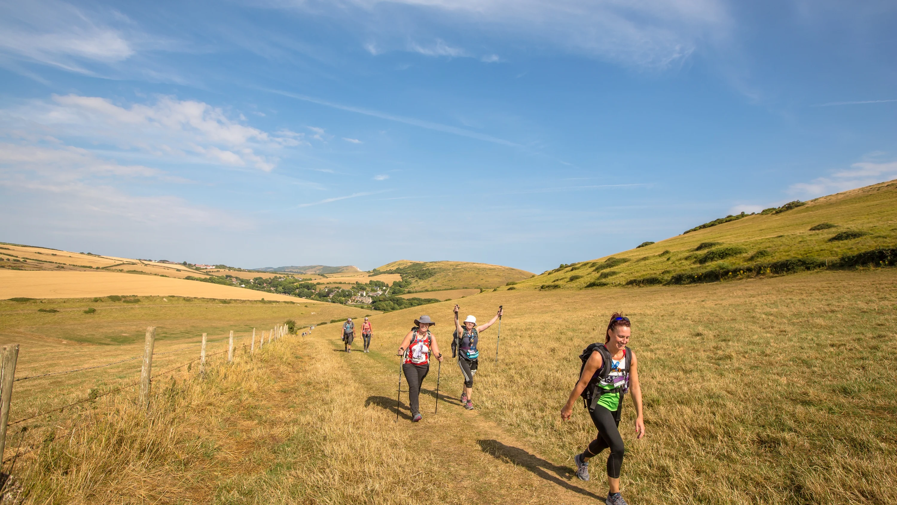 Five people walking across an open field with buildings and hills in the background.