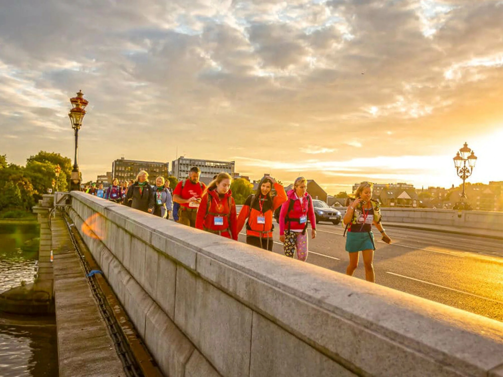 A large group of people walking along London's Putney bridge while the sun sets in the background.