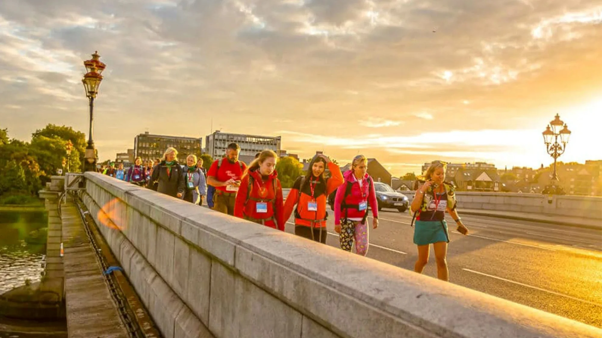 A large group of people walking along London's Putney bridge while the sun sets in the background.