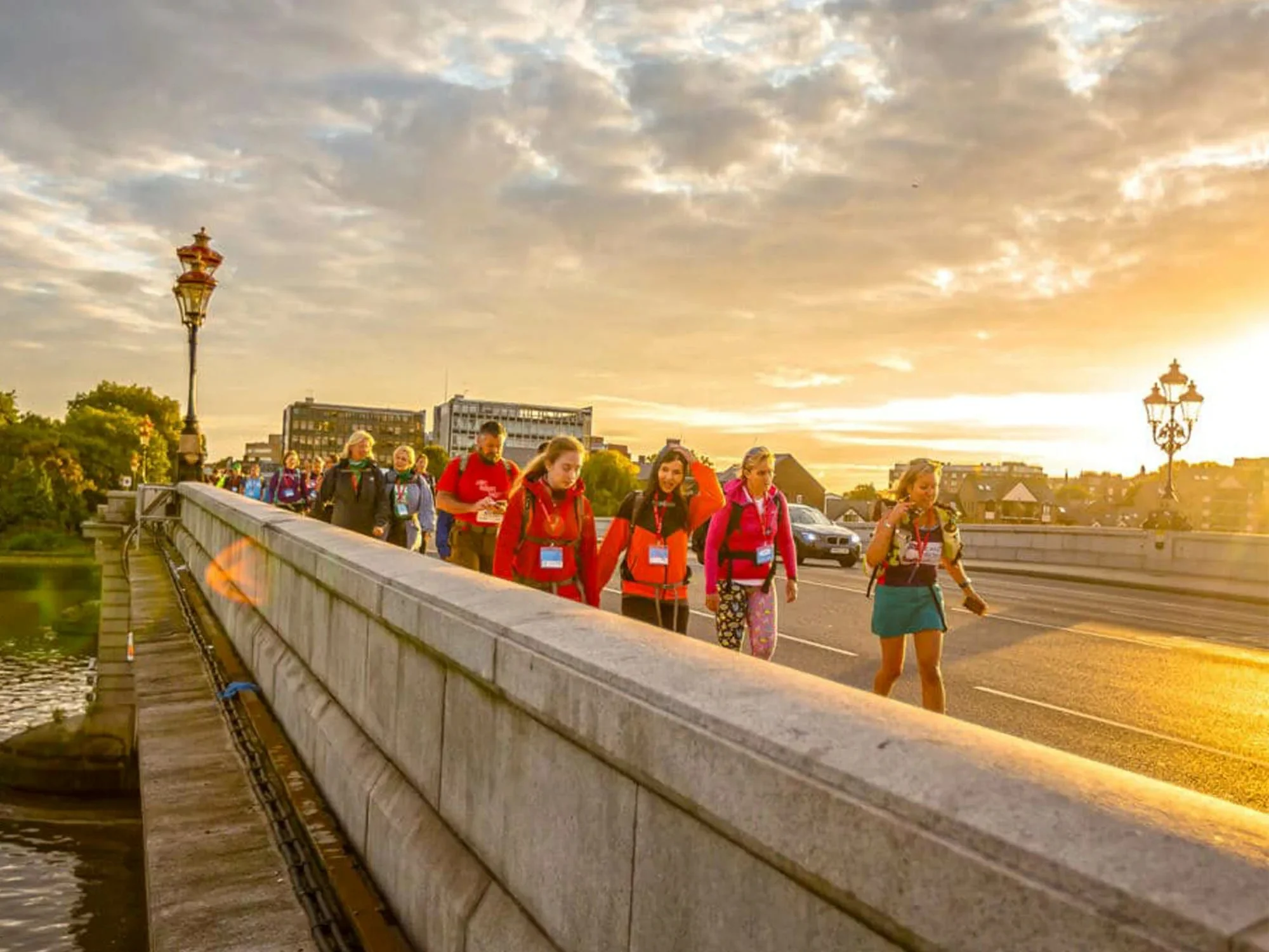 A large group of people walking along London's Putney bridge while the sun sets in the background.