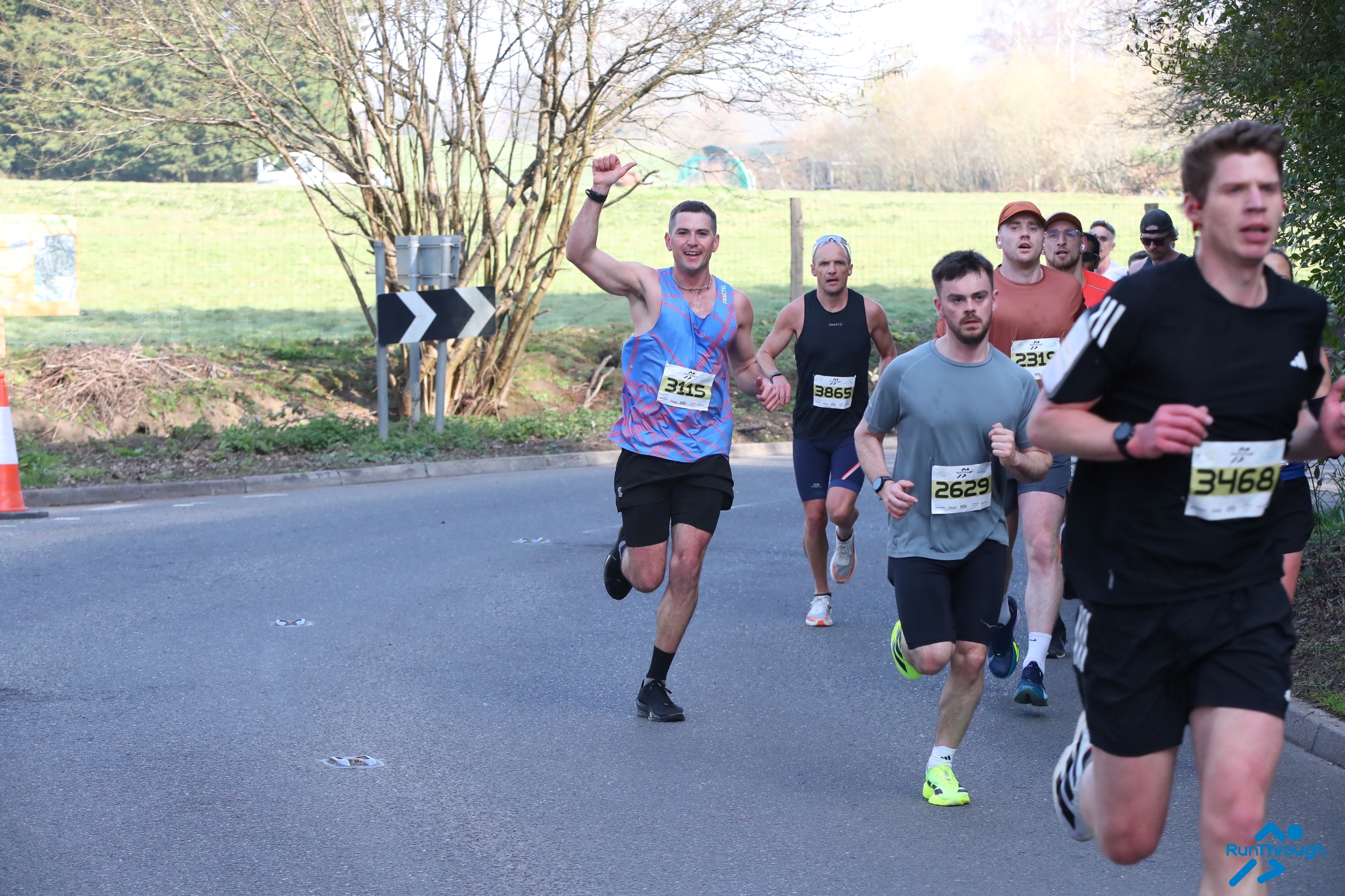 A group of runners running on the road with a field behind them at the Surrey Half Marathon.