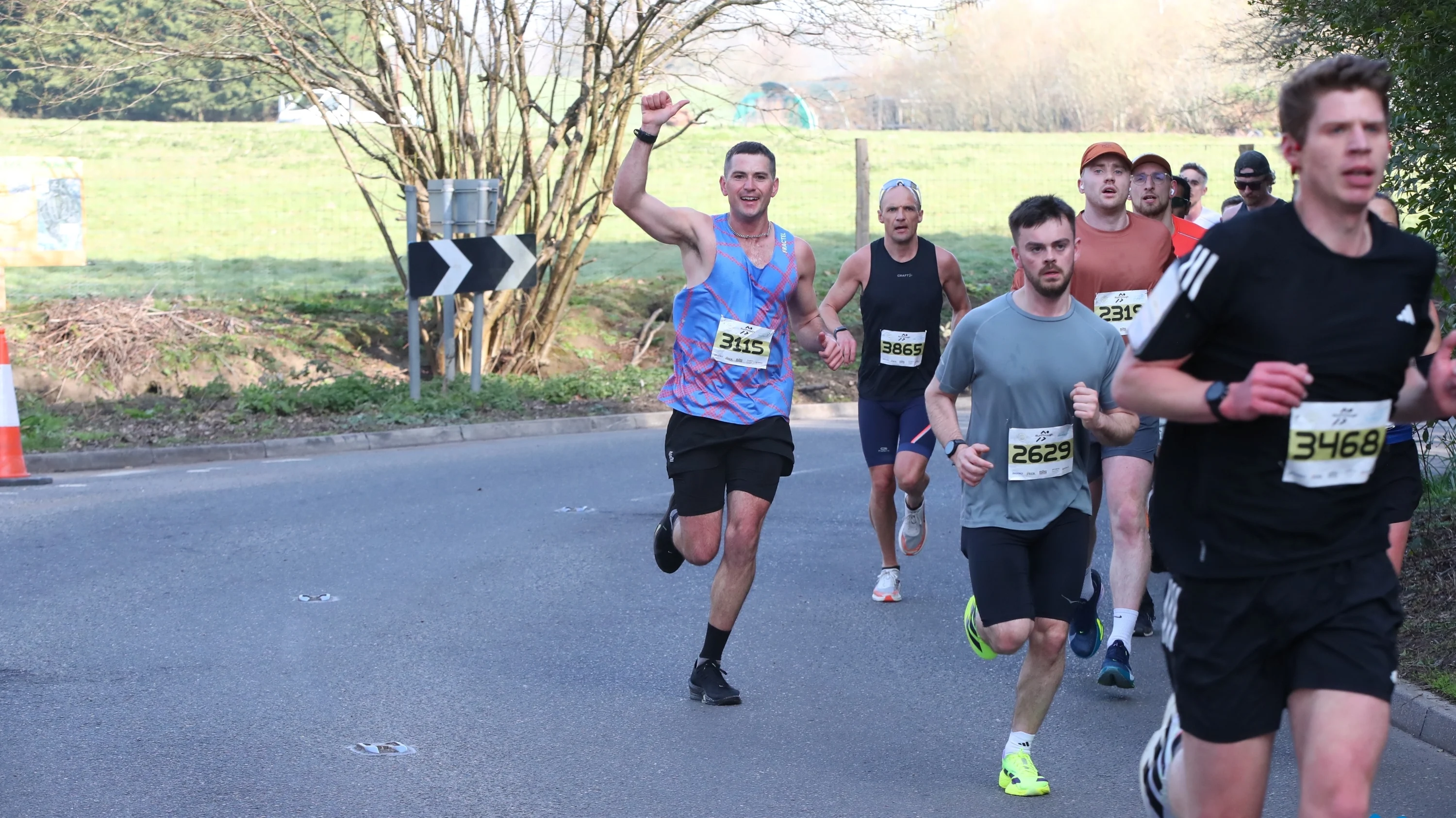 A group of runners running on the road with a field behind them at the Surrey Half Marathon.