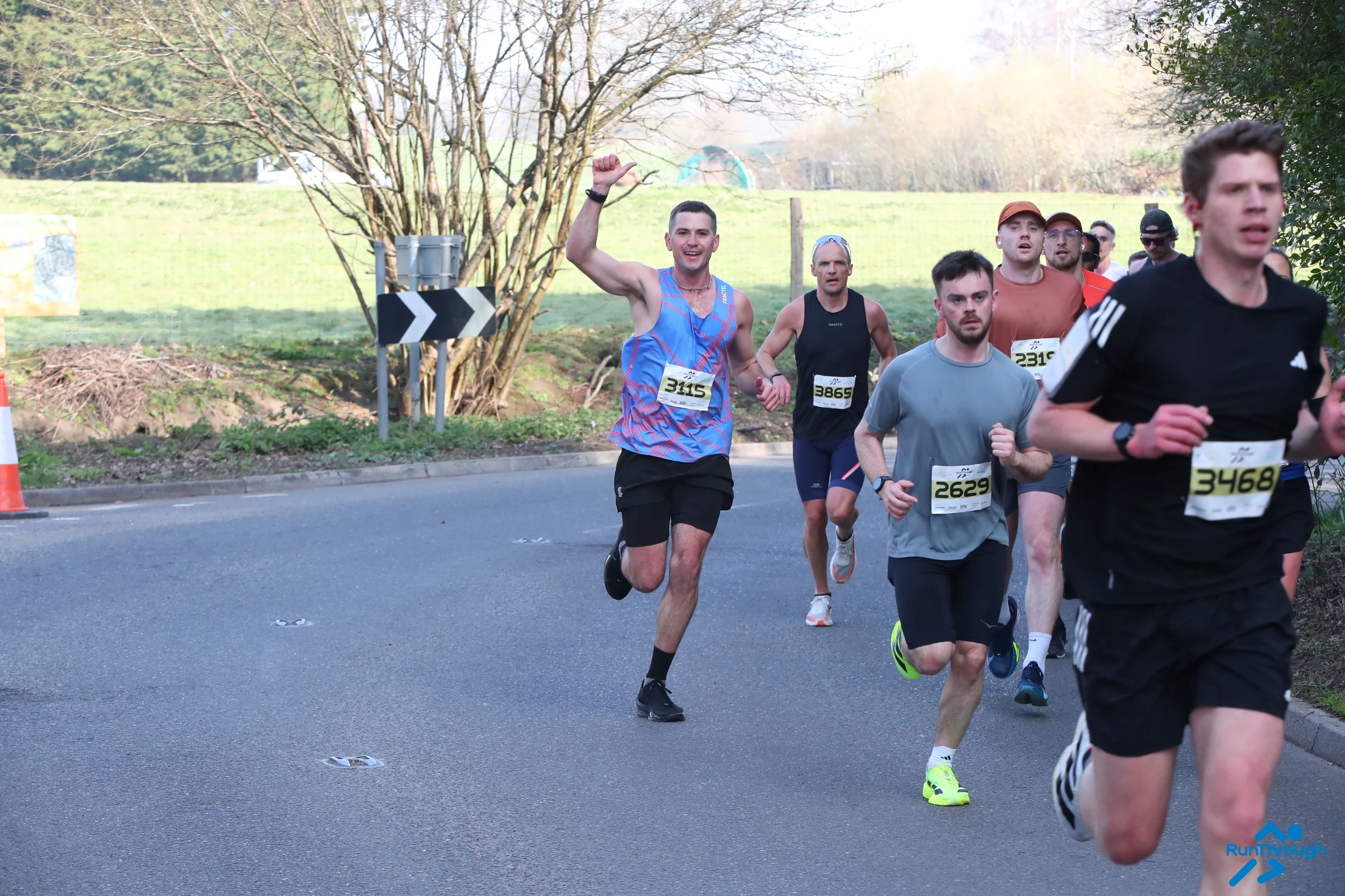 A group of runners running on the road with a field behind them at the Surrey Half Marathon.