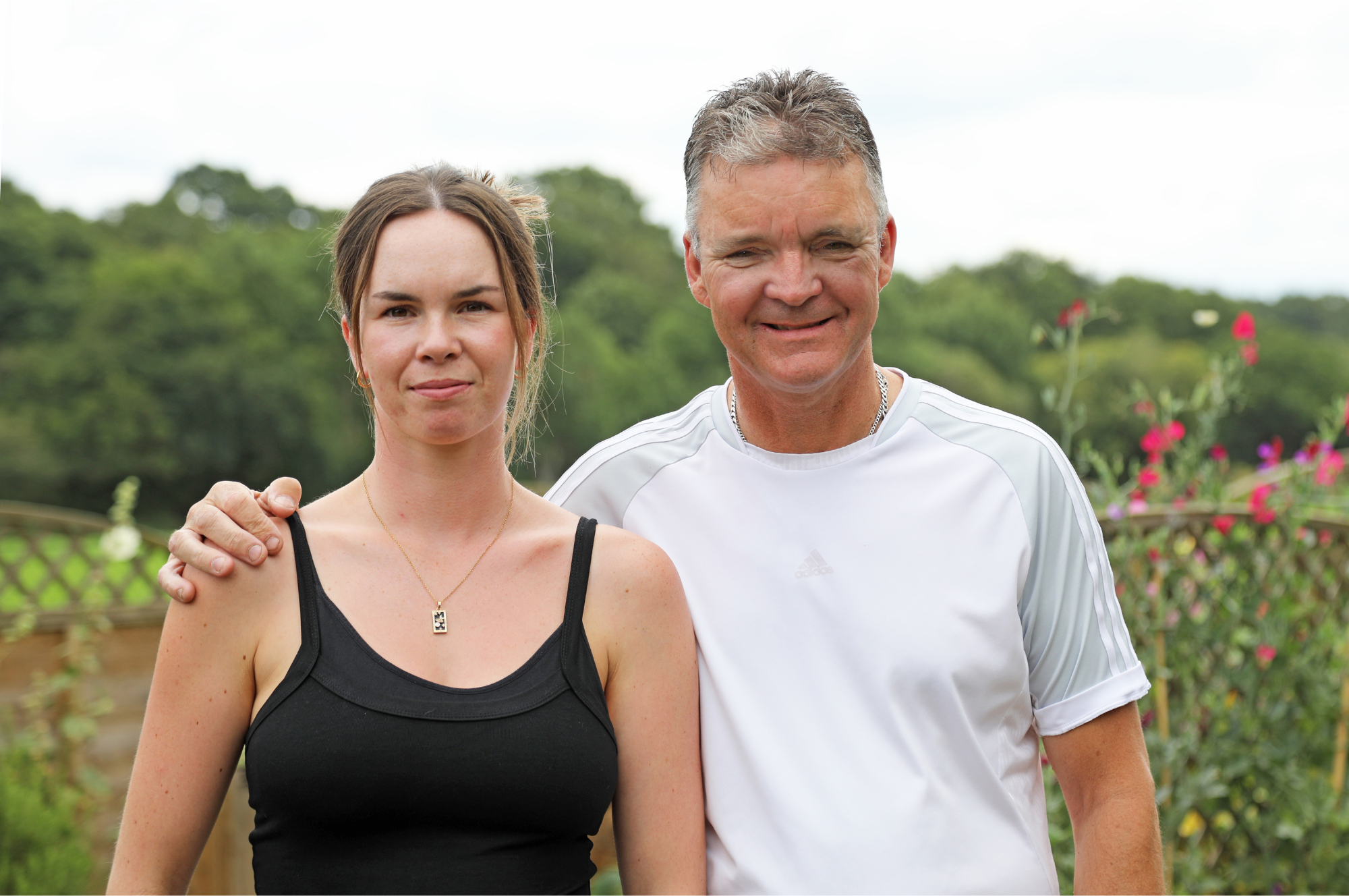 A photograph of Olivia and Gary Pitfield smiling in a garden. Gary has his arm around Olivia.