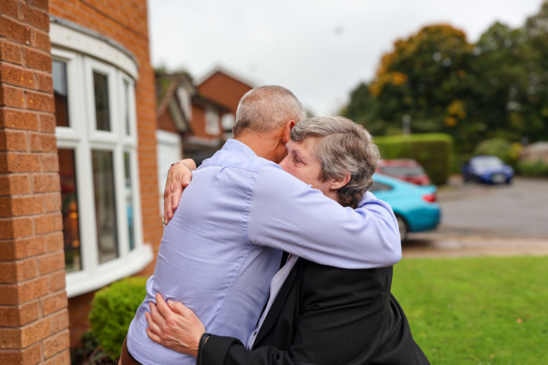 A photograph of Danny and Suzanne hugging outside a house.
