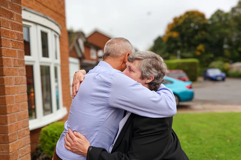 A photograph of Danny and Suzanne hugging outside a house.